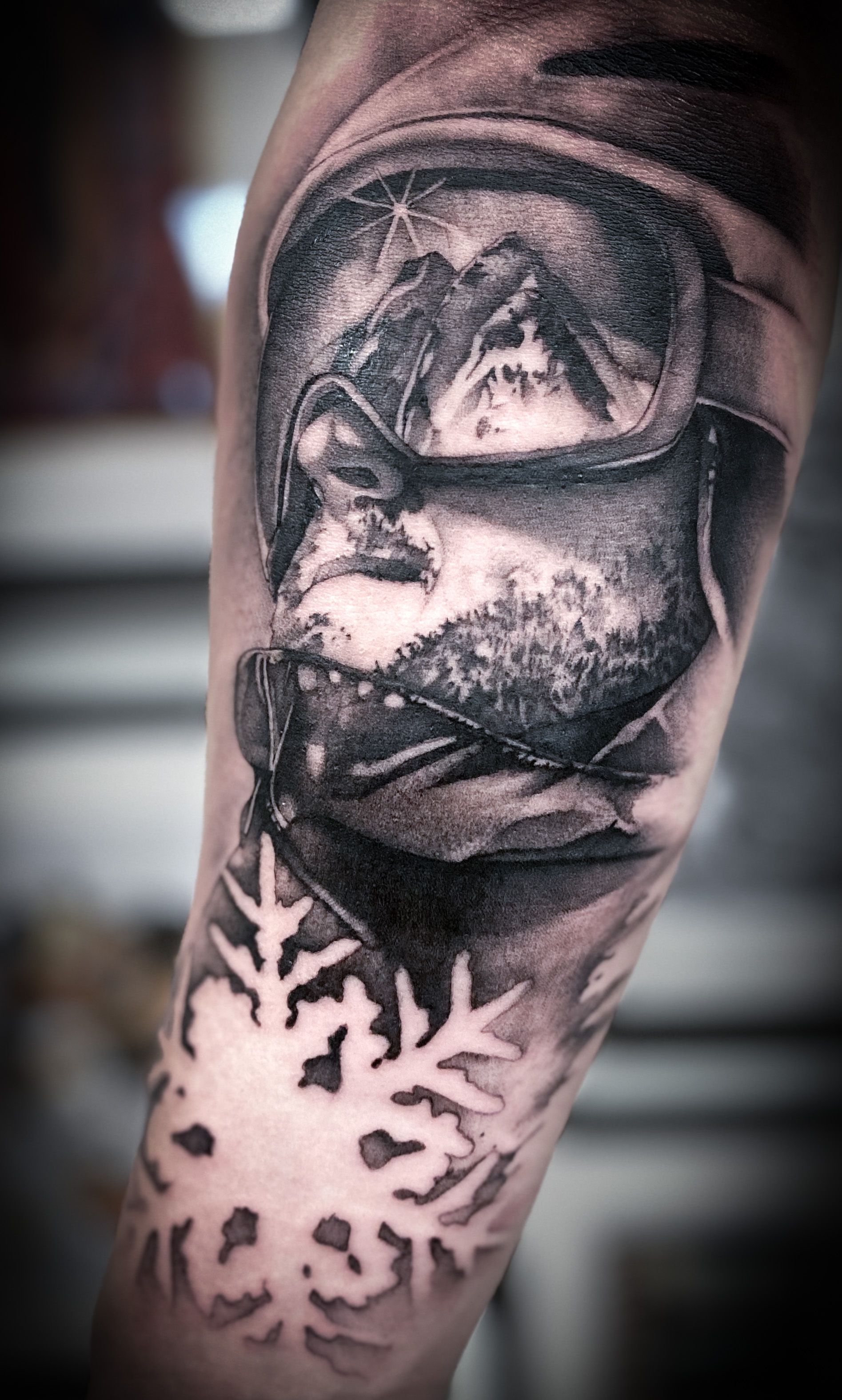 Ein schwarz-weißes Tattoo eines Mannes mit Schutzbrille und einer Schneeflocke.