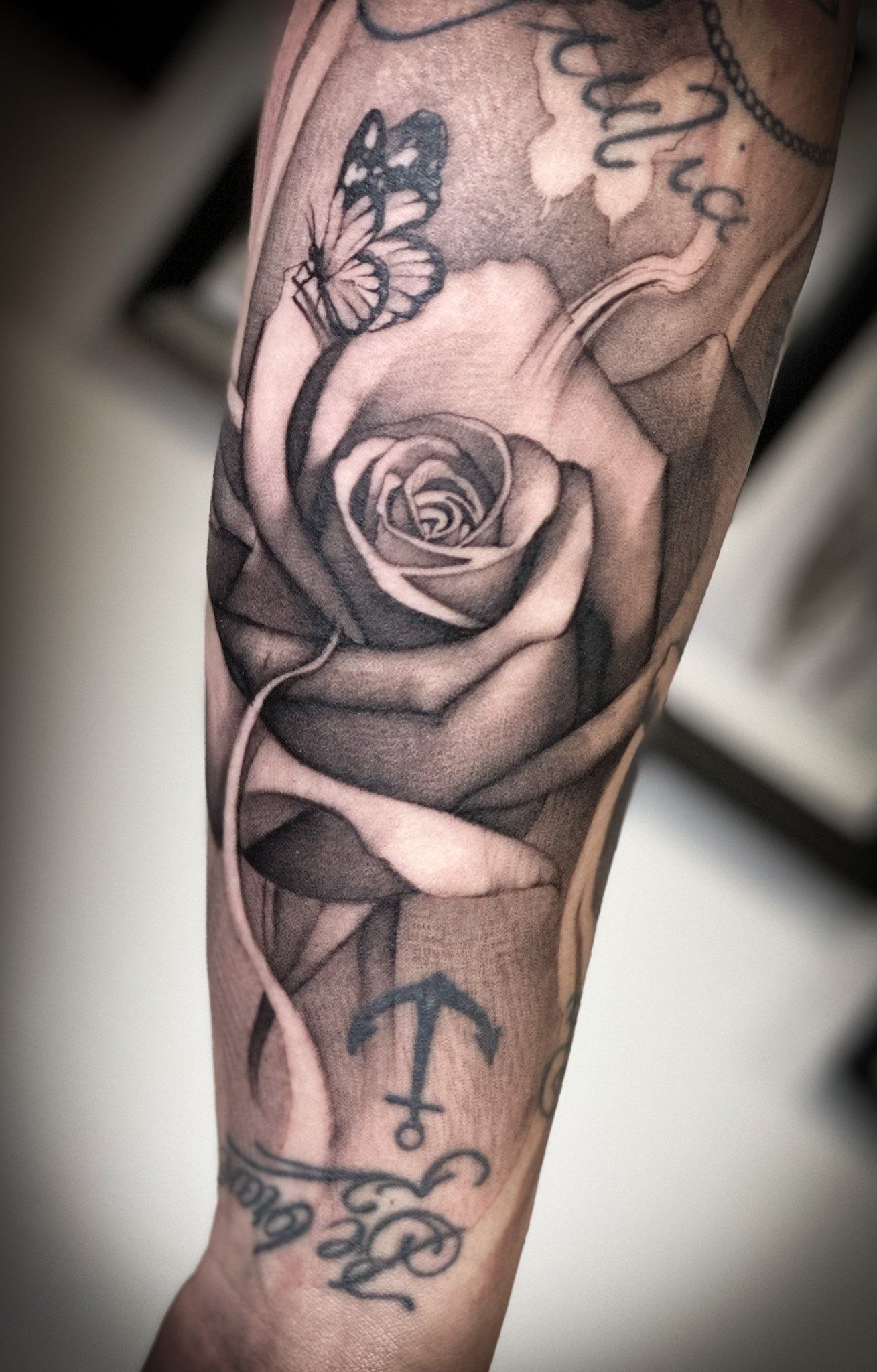 Eine schwarz-weiße Tätowierung einer Rose und eines Schmetterlings auf dem Arm einer Person.