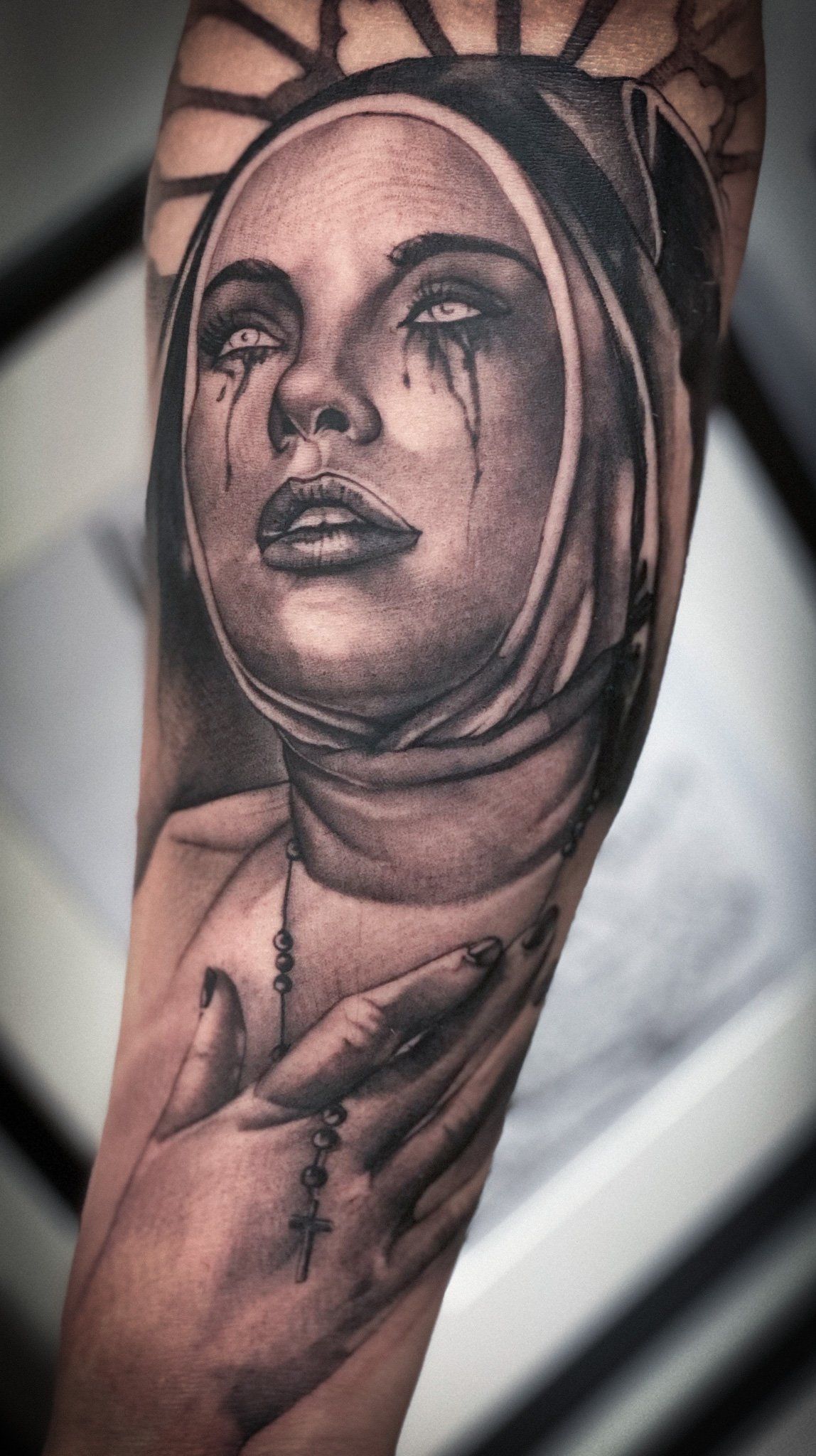 Ein schwarz-weißes Tattoo einer Nonne mit einem Kreuz auf ihrem Unterarm.