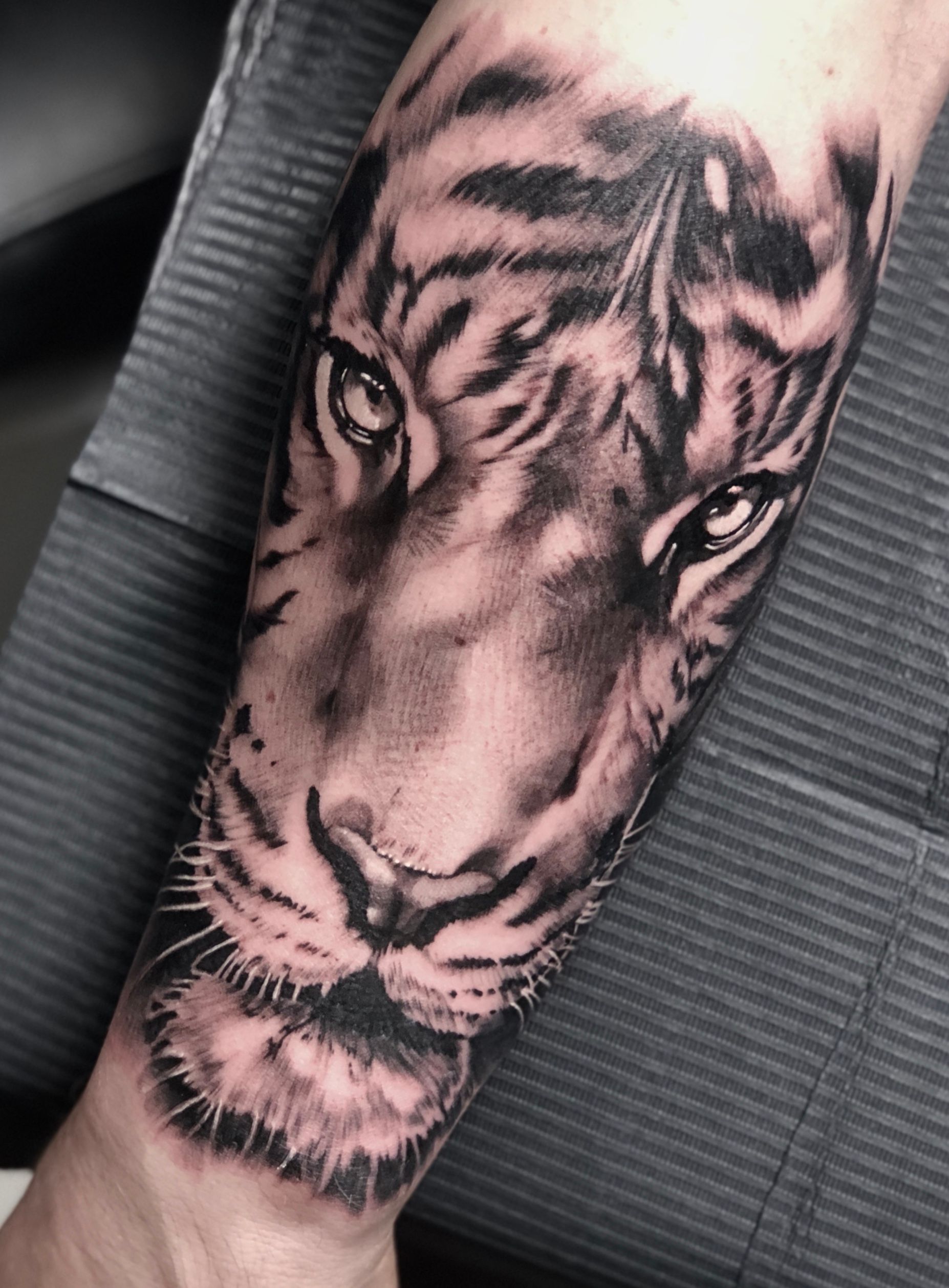 Eine schwarz-weiße Tätowierung eines Tigerkopfes auf dem Unterarm einer Person.