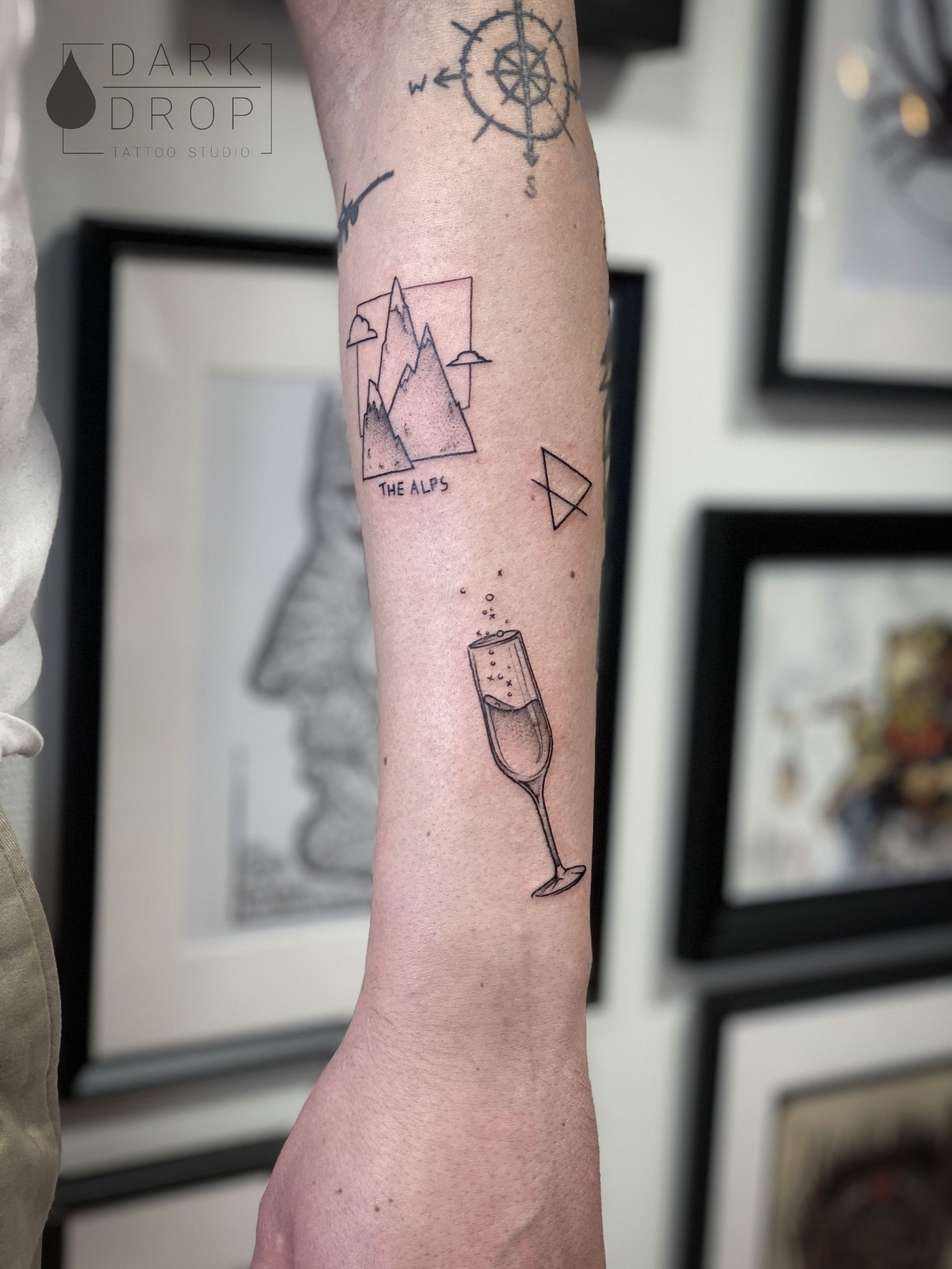 Eine Person hat ein Tattoo mit einem Weinglas und einem Kompass auf dem Arm.