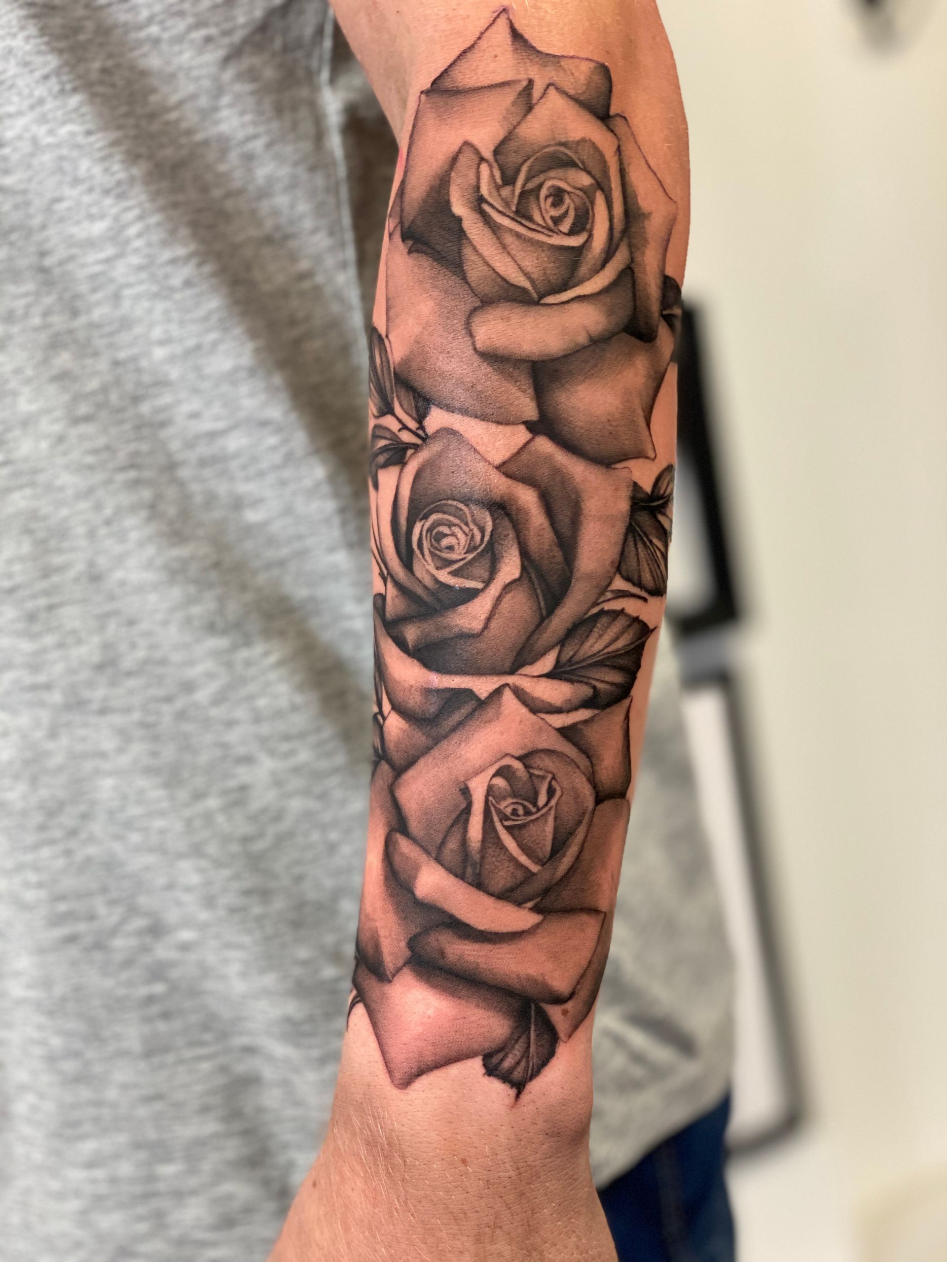 Ein Mann hat eine Tätowierung mit drei Rosen auf seinem Unterarm.