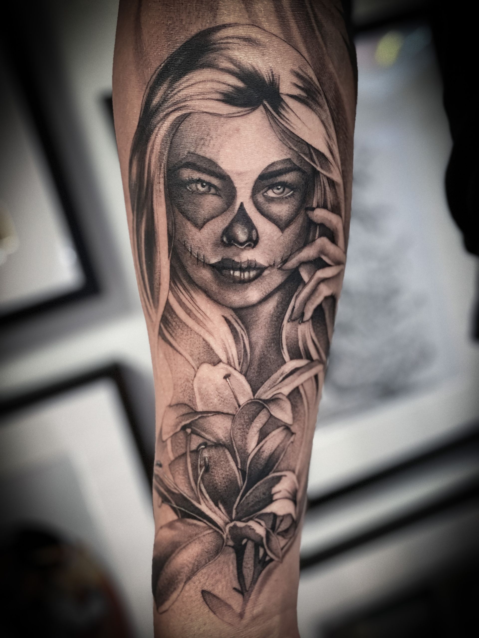 Ein schwarz-weißes Tattoo einer Frau mit einem Totenkopf im Gesicht und Blumen.