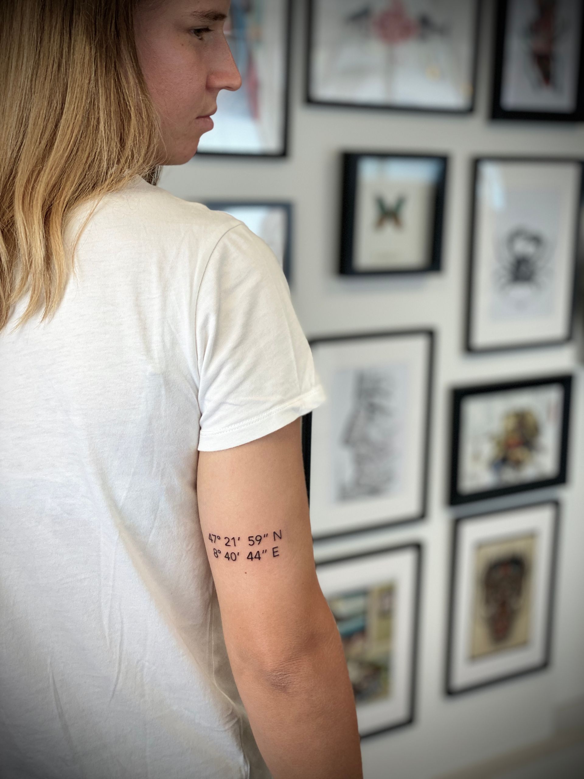 Eine Frau hat eine Tätowierung auf ihrem Arm mit der Aufschrift „GPS-Koordinaten“.