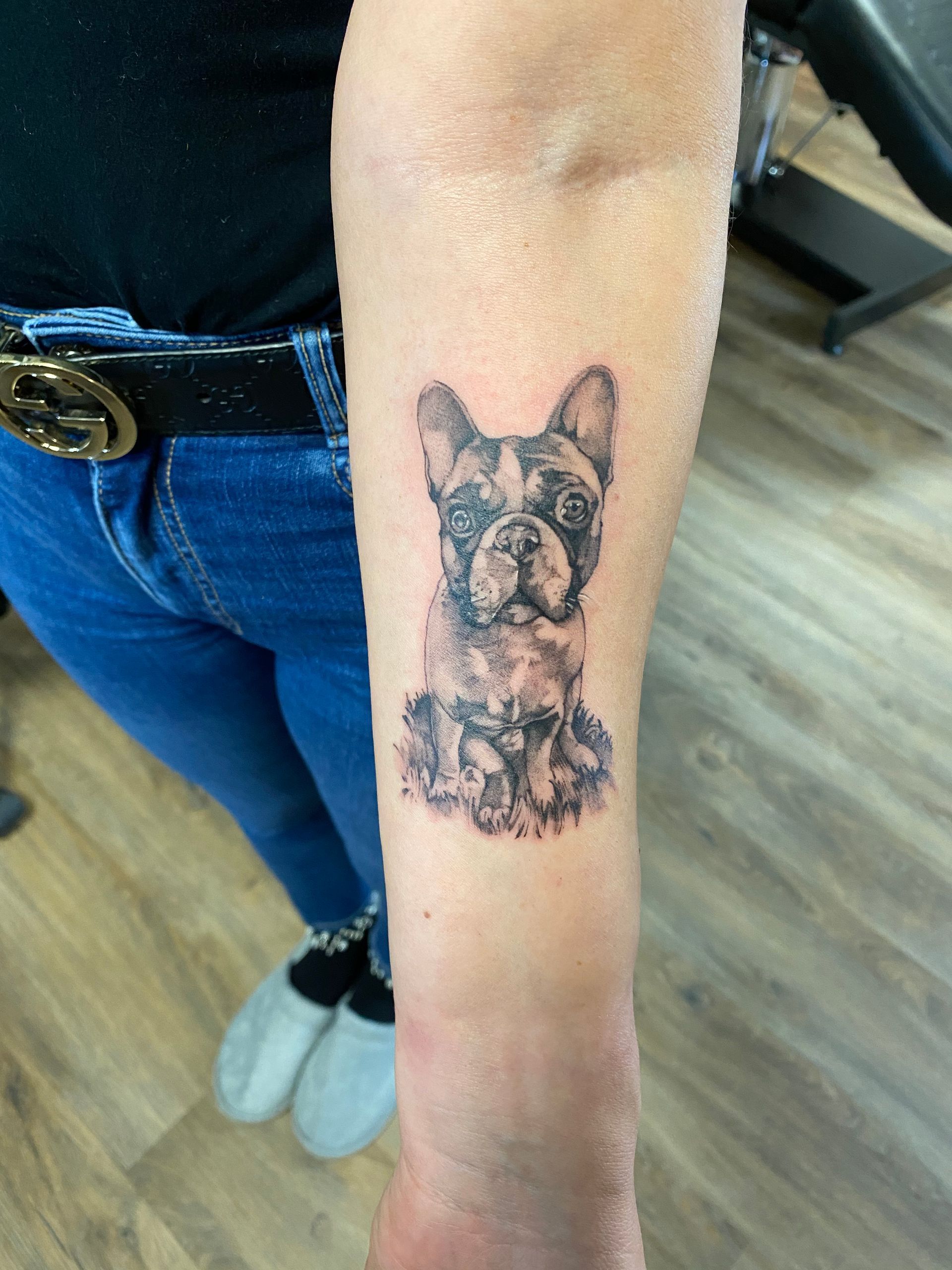 Eine Frau hat eine Tätowierung einer französischen Bulldogge auf ihrem Unterarm.