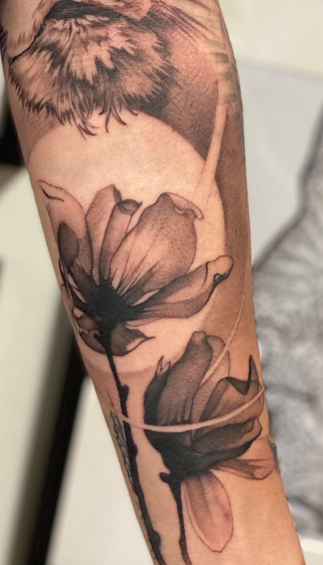 Eine schwarz-weiße Tätowierung einer Blume auf dem Unterarm einer Person.