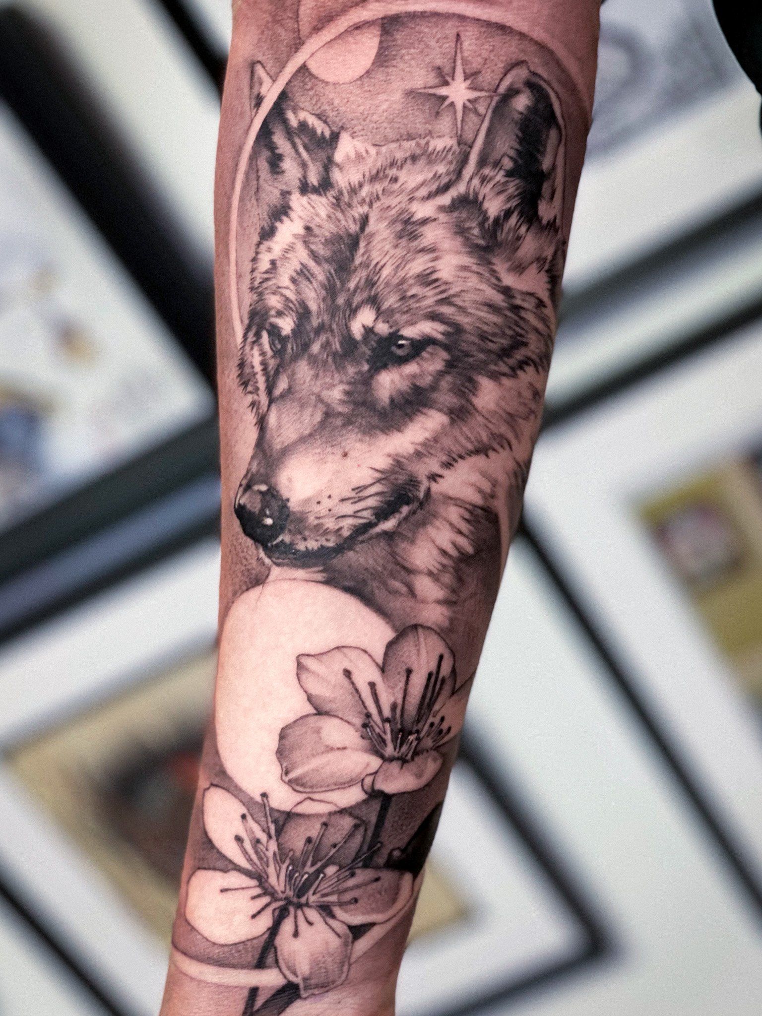 Ein Tattoo von einem Wolf und Blumen auf dem Arm einer Person