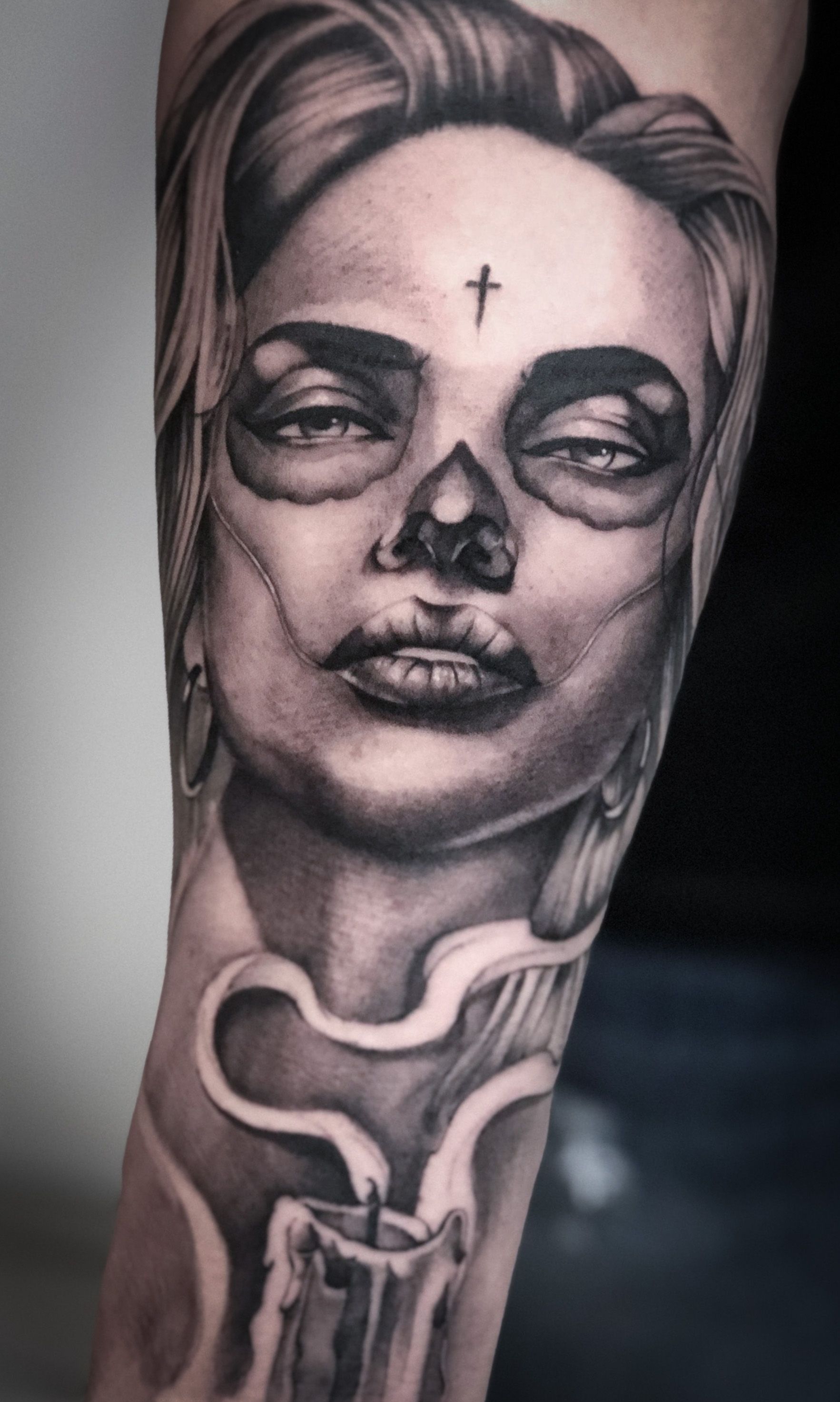 Ein schwarz-weißes Tattoo einer Frau mit einem Kreuz auf der Stirn und einer Kerze.