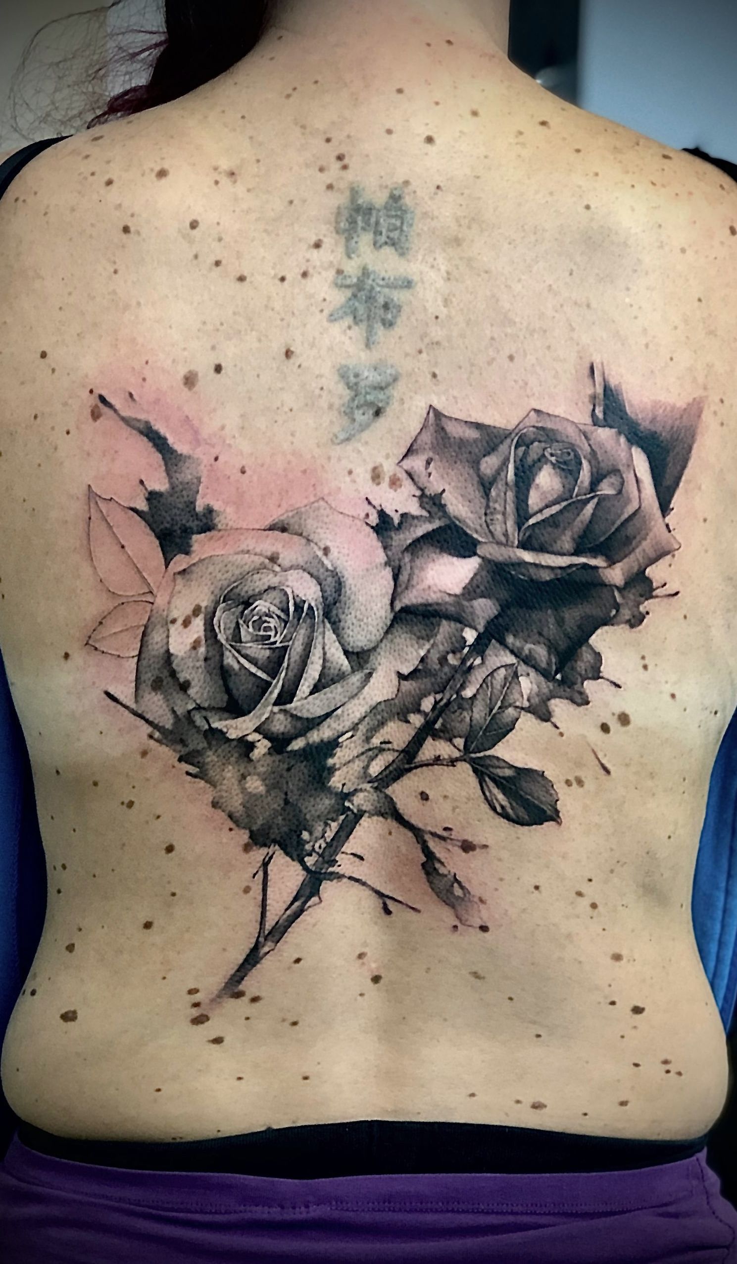 Eine Frau hat eine Tätowierung mit zwei Rosen auf ihrem Rücken.