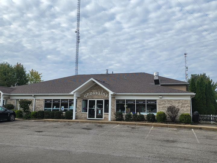 Low brick building with a central entrance, gravel lot, and cloudy sky above