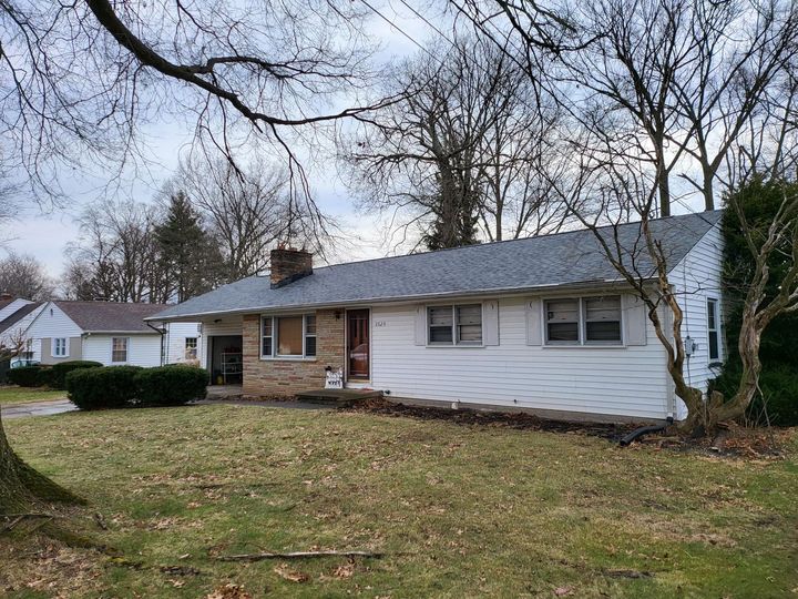 Single-story suburban house with white siding, brick porch, and leafless trees in a front yard