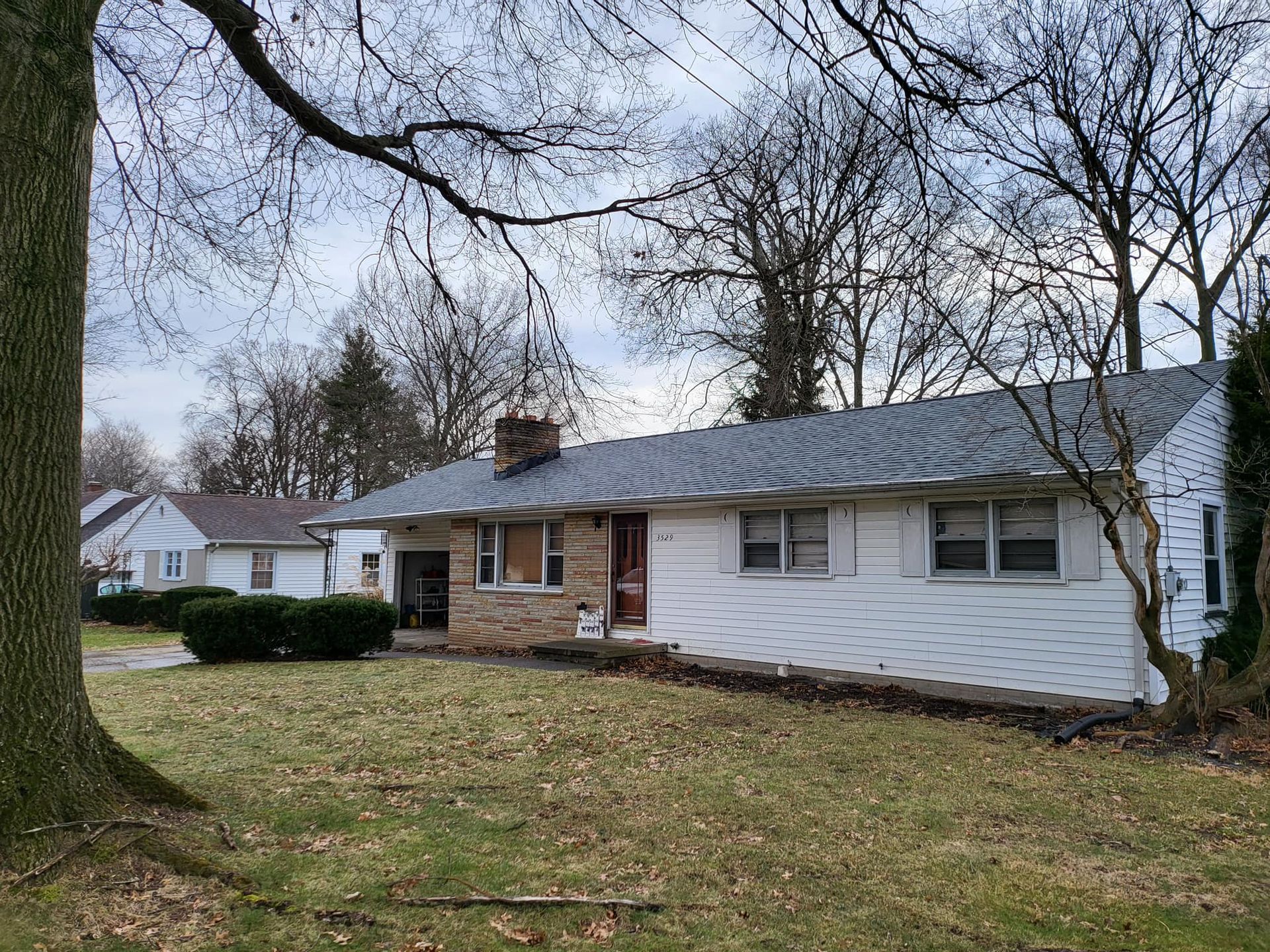 Single-story white house with stone front and large front yard under leafless trees