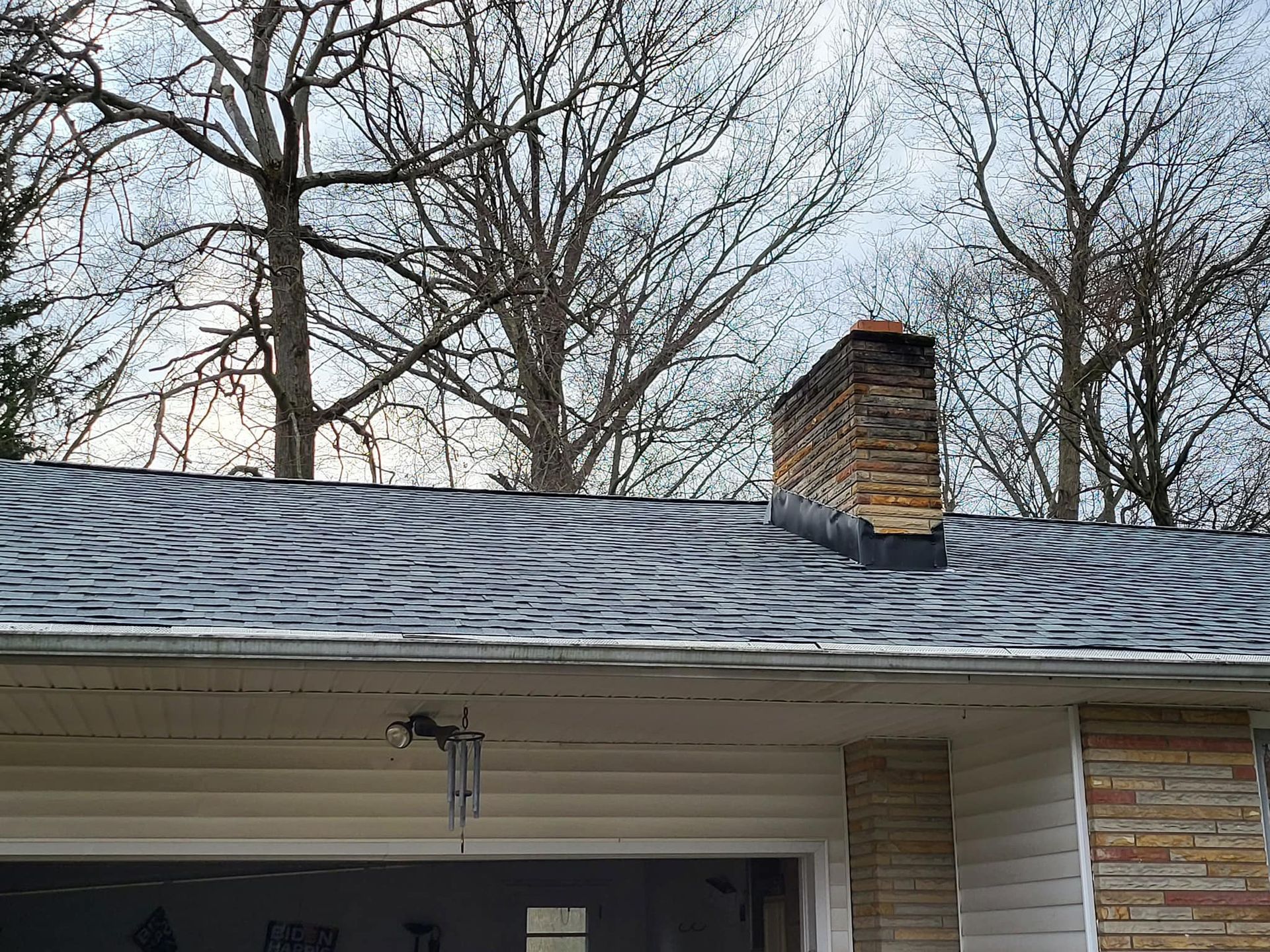 Snow-dusted roof with a brick chimney and bare trees in the background