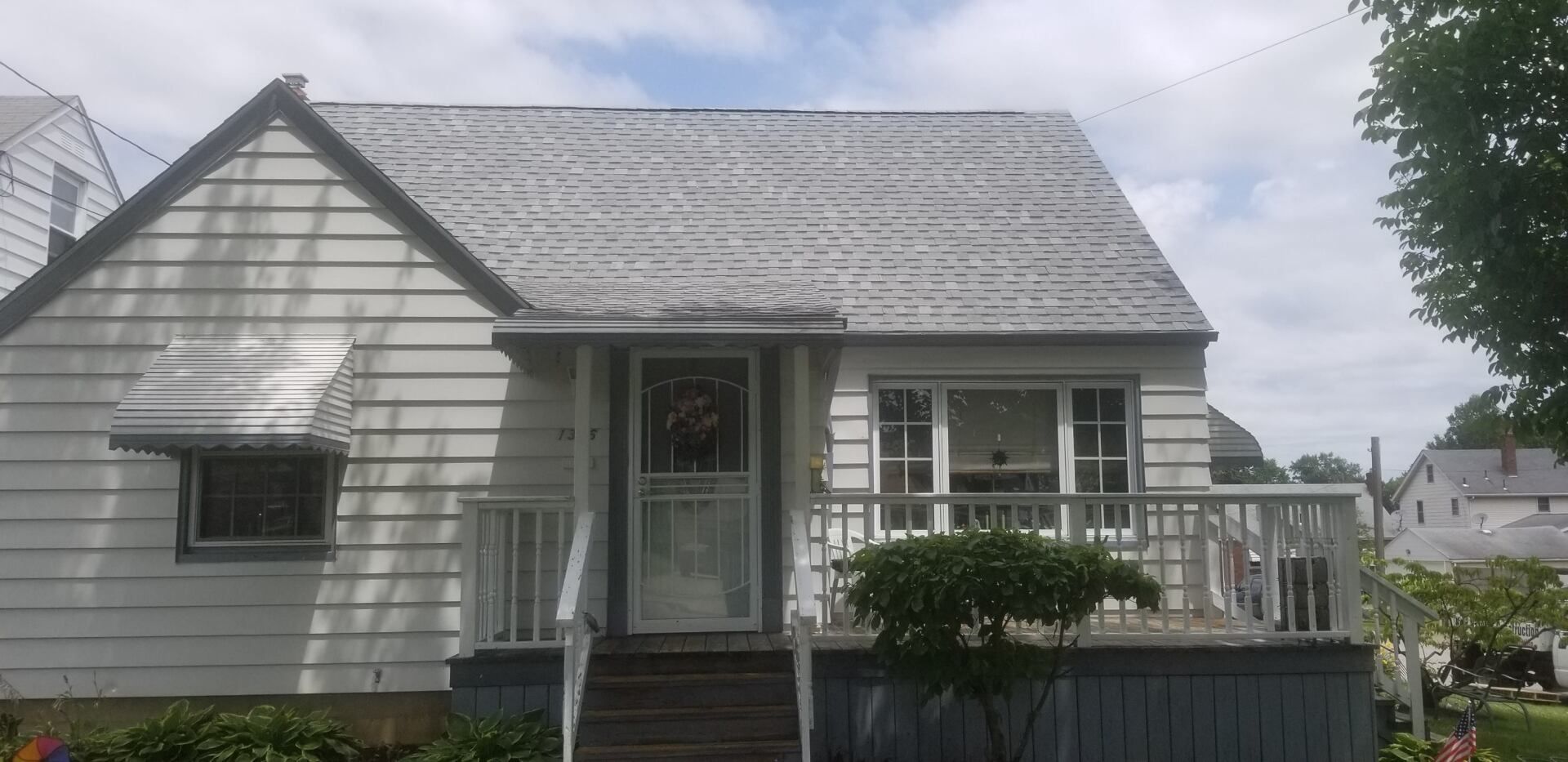 Small white house with gray roof, front porch, and a small green hedge by the door