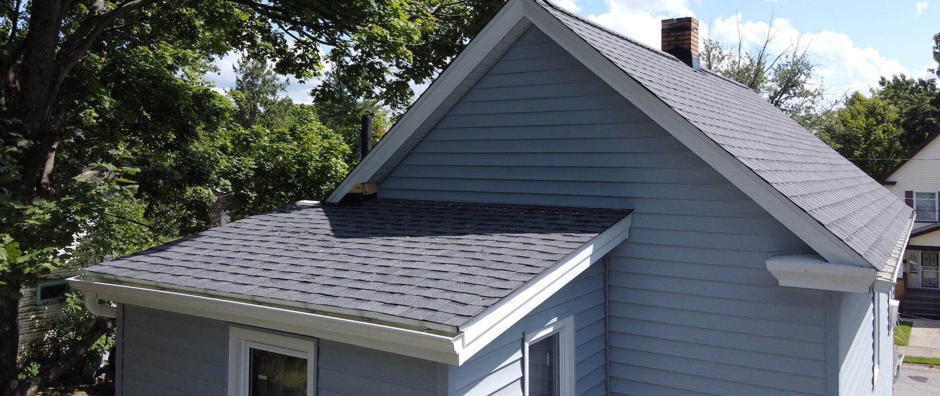Gray shingled roof with blue house siding and trees in the background