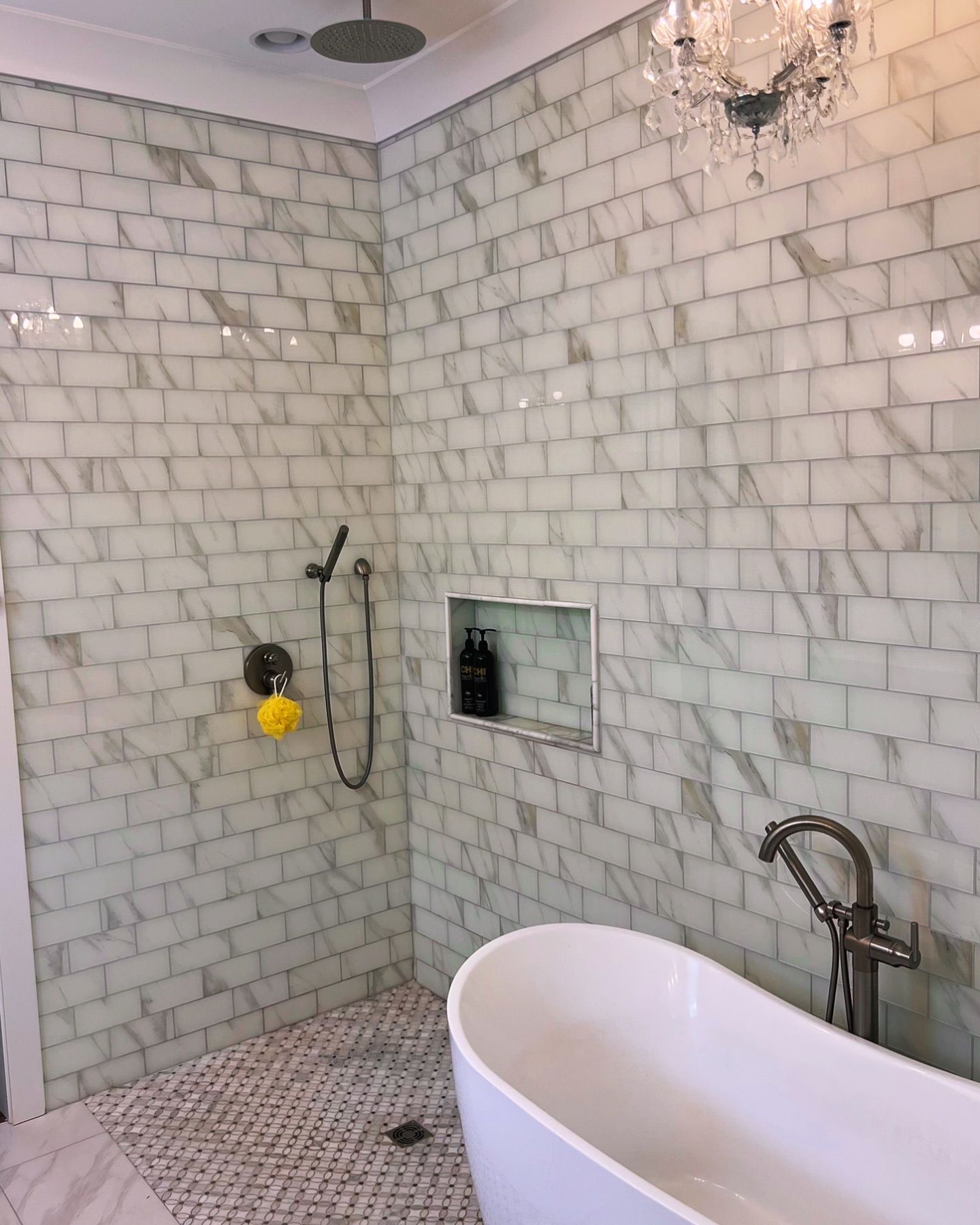 A bathroom with a tub , shower , and chandelier.