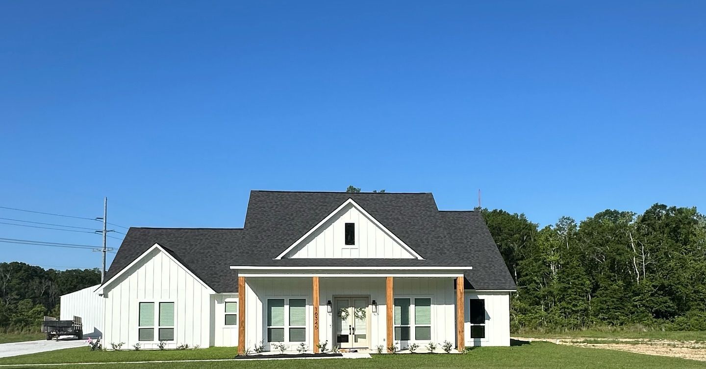 A white house with a black roof is sitting on top of a lush green field.