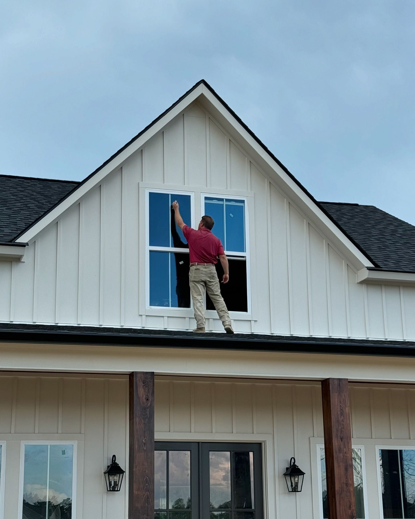 A man is standing on the roof of a house cleaning a window.