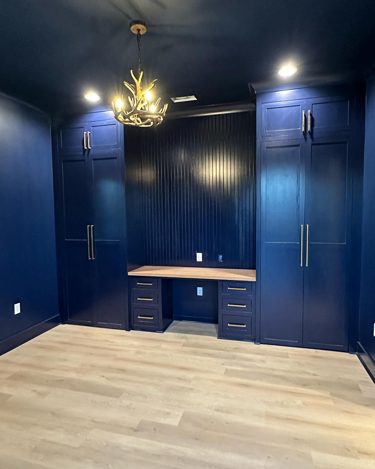 A room with blue walls , blue cabinets , a desk and a chandelier.