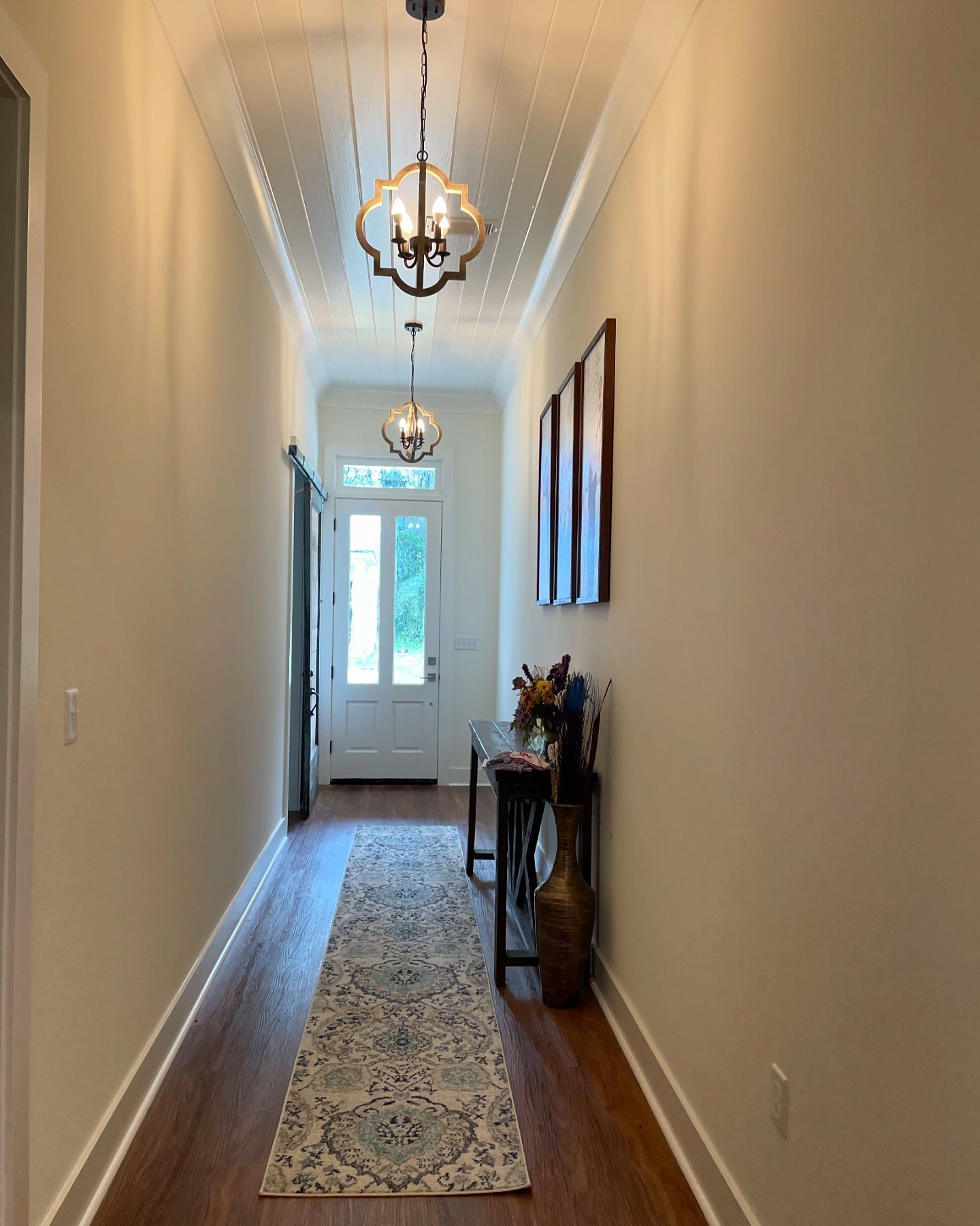 A long hallway with a table in the middle and a rug on the floor.