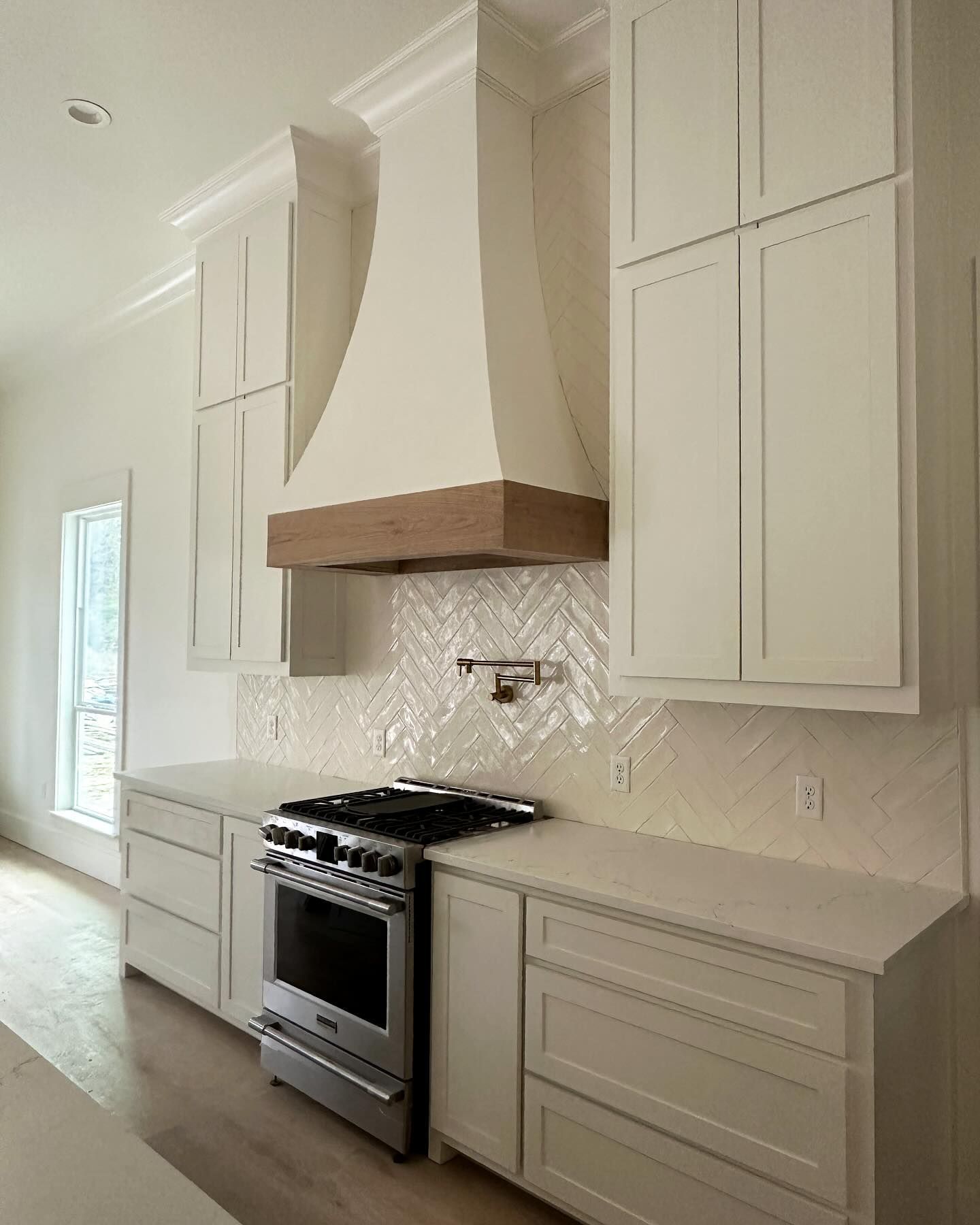 A kitchen with white cabinets , a stove , and a hood.