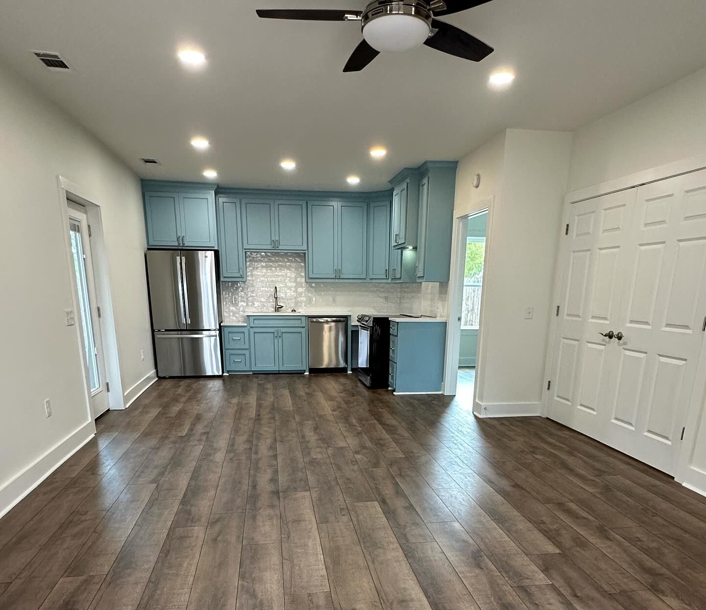 A kitchen with blue cabinets , stainless steel appliances and a ceiling fan.
