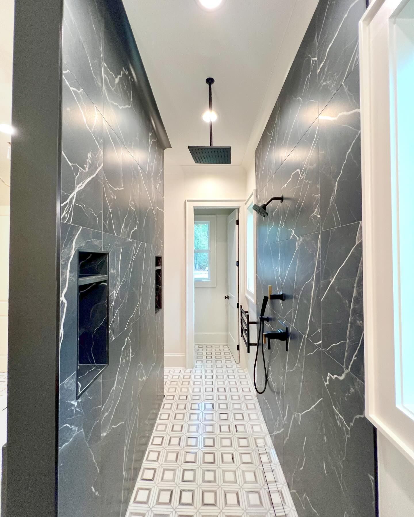 A hallway in a bathroom with marble walls and a shower.