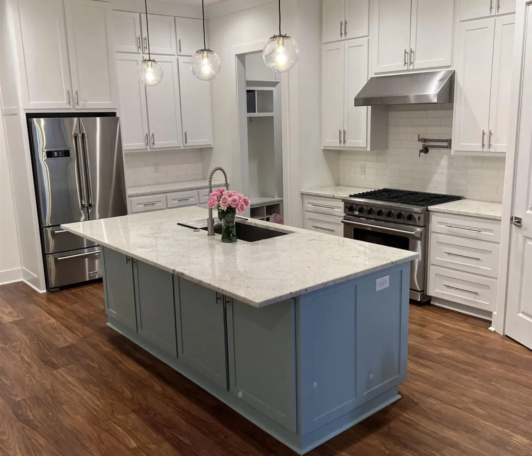 A kitchen with white cabinets , stainless steel appliances , a large island and a sink.