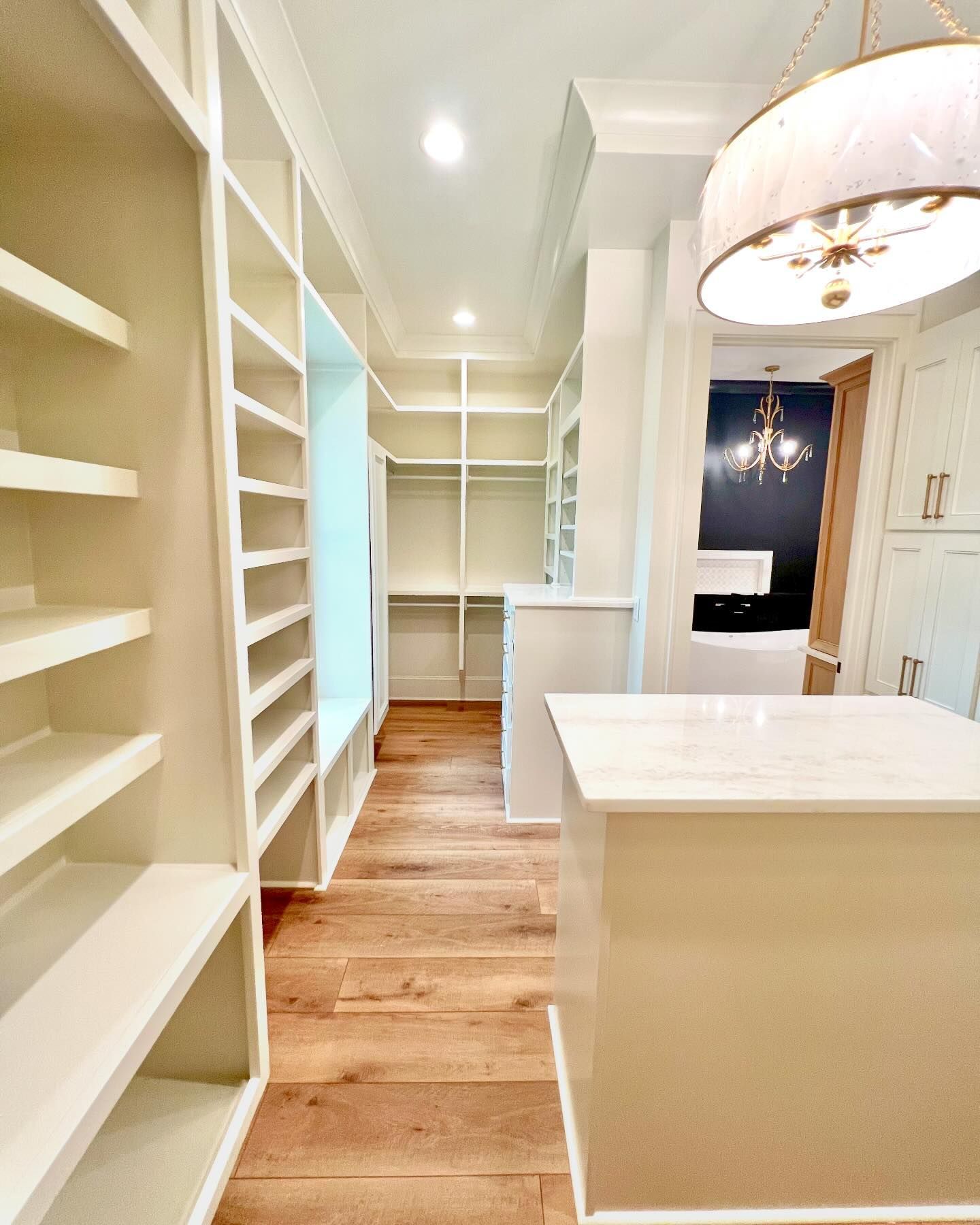 A walk in closet with lots of shelves and a large island in the middle.