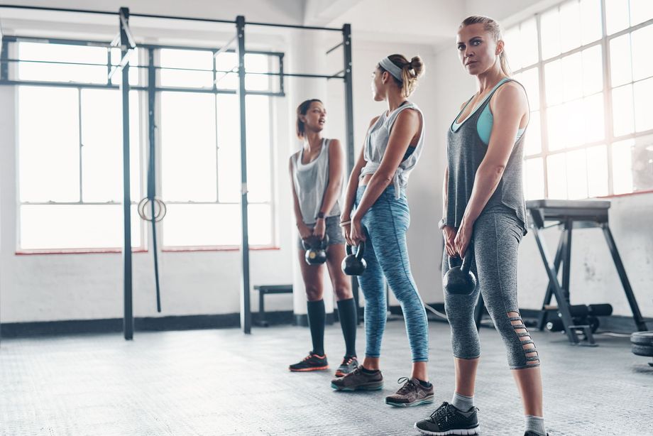 Tre donne in palestra tengono in mano dei kettlebell e si preparano per l'allenamento.