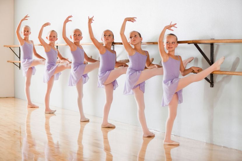 Sei giovani ballerine in body e gonne color lavanda, che si allungano alla sbarra.