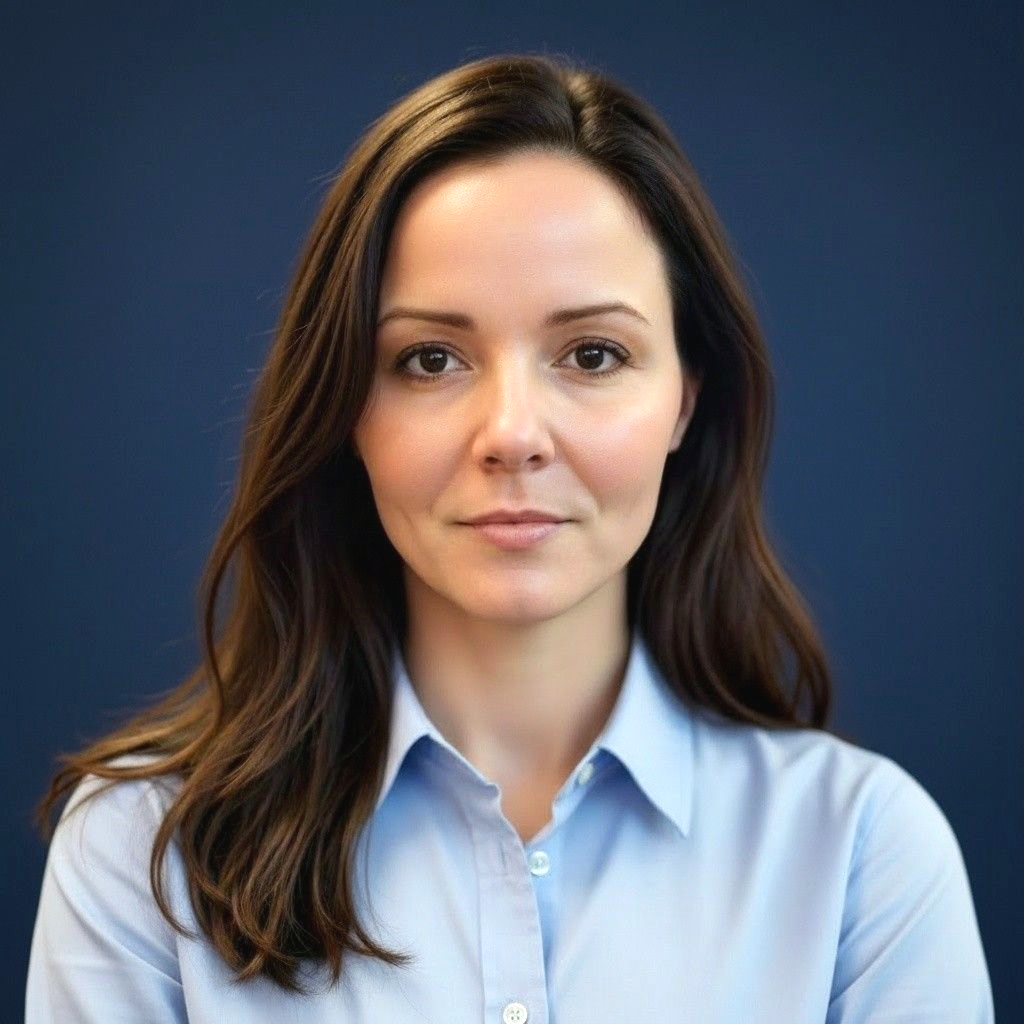 Woman with brown hair in a dark blue top, looking directly at the camera with a neutral expression.