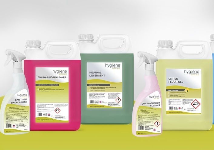 Cleaning products, various colors, including spray bottles and large jugs, on a light green surface.