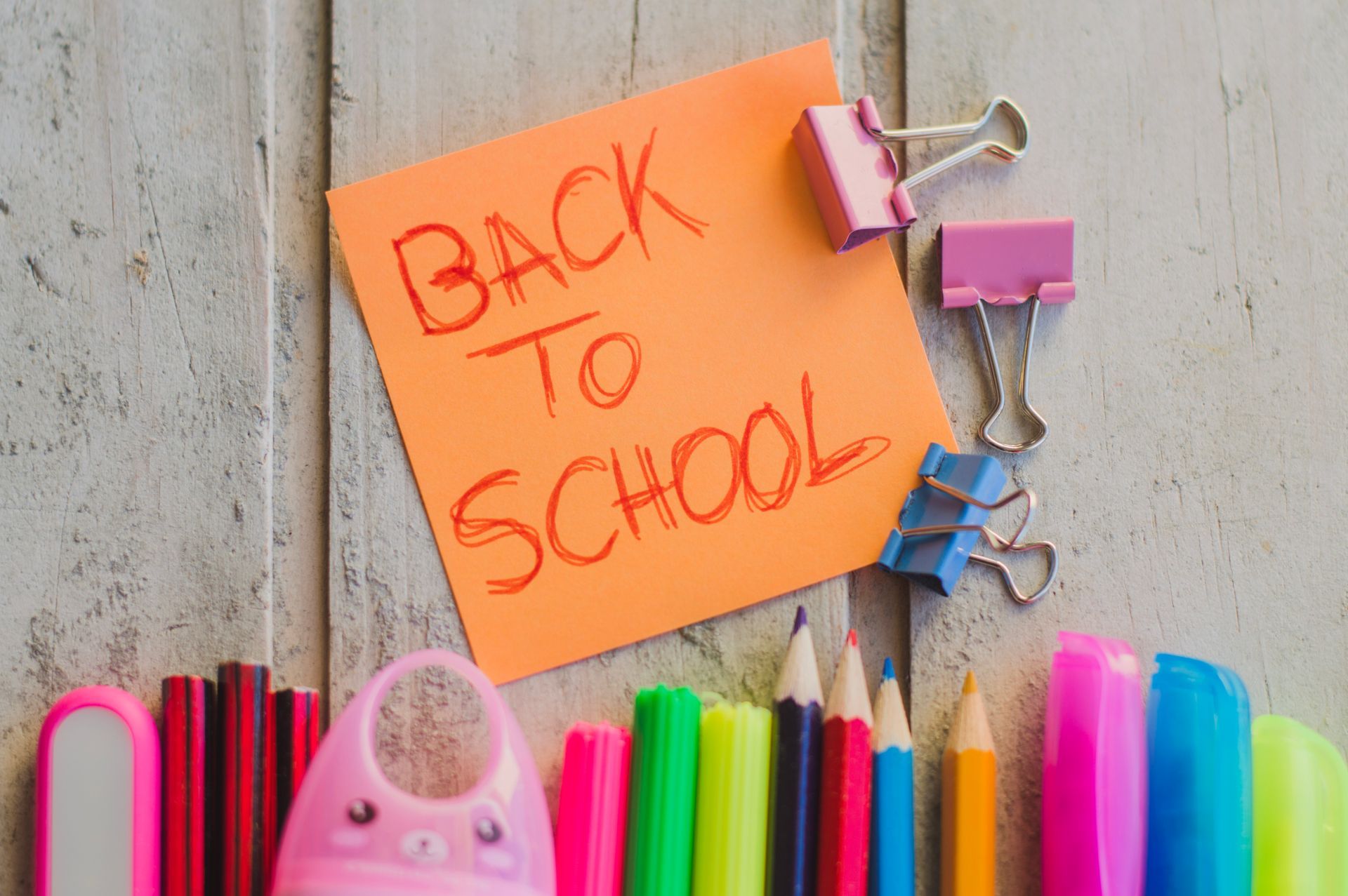 Back to school note with colorful pencils and a pink sharpener on a wooden background