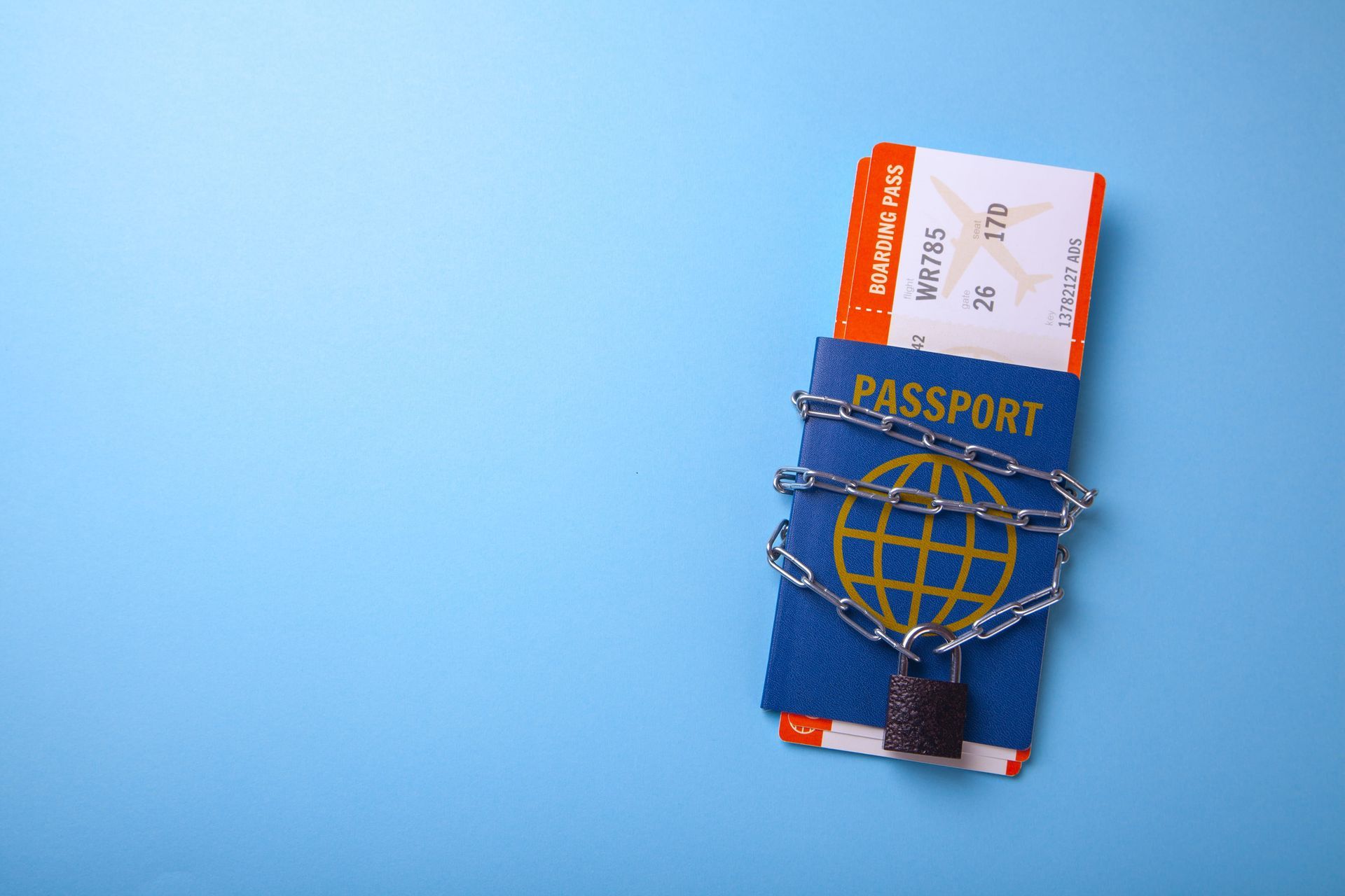 Blue passport with boarding pass secured by a globe strap on a light blue background