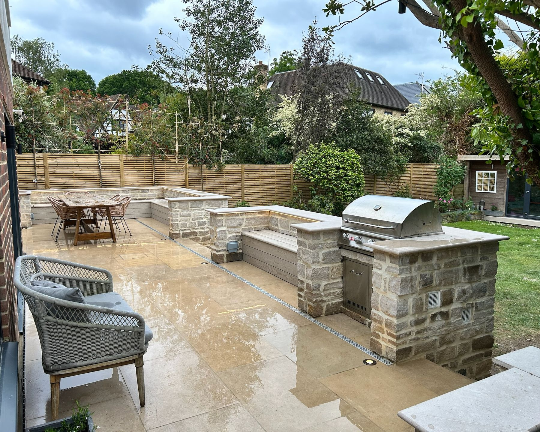 Outdoor patio with built-in grill, seating, and table; wooden fence in background.
