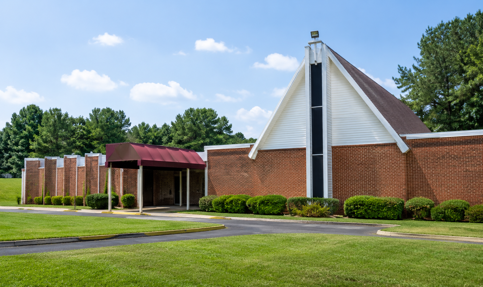 Brick church with white triangular entrance, red roof, and green lawn under a blue sky