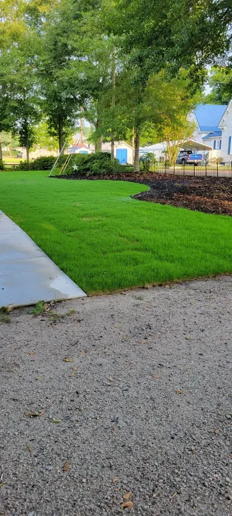 Front yard with newly laid green sod beside a dirt driveway and a brick house
