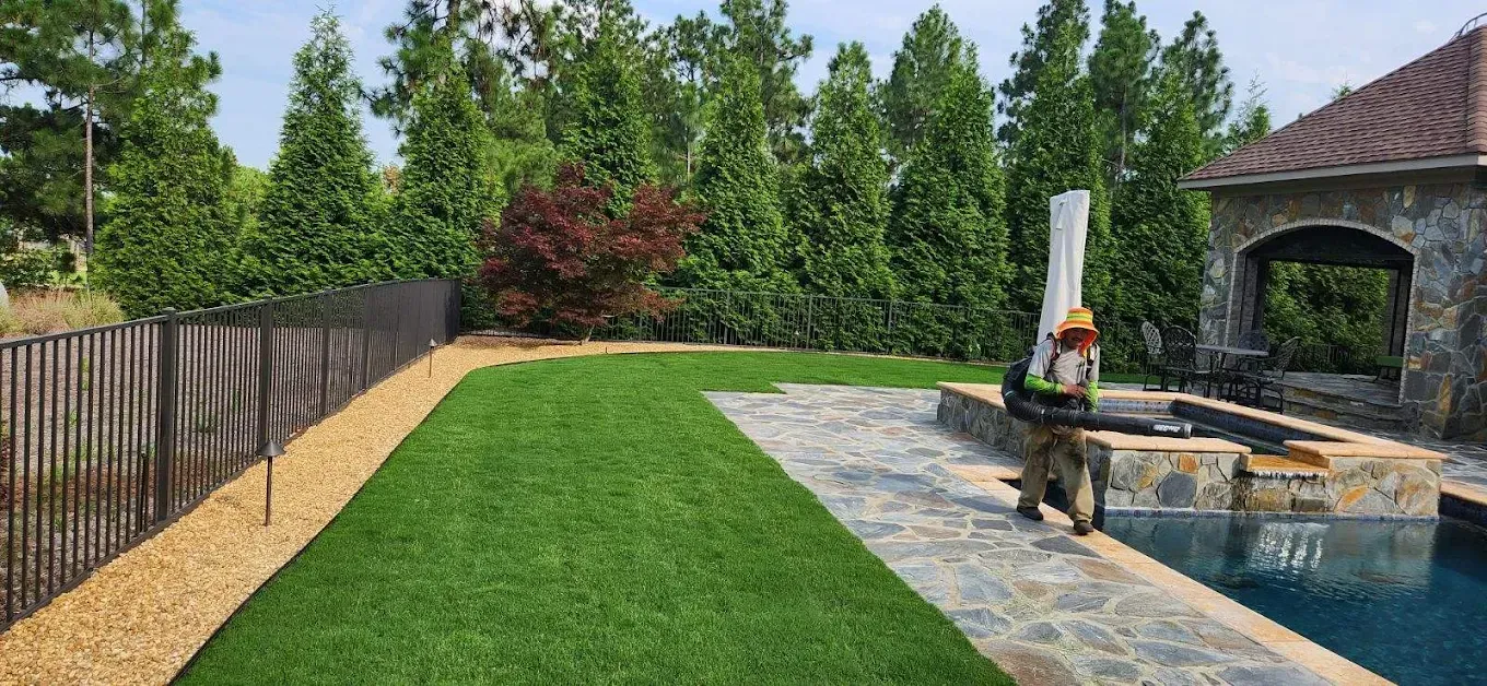 Spacious green backyard lawn enclosed by a wooden fence, with trees in the background.