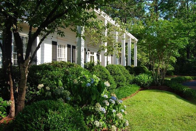 White house with columns and lush green garden in bright sunlight
