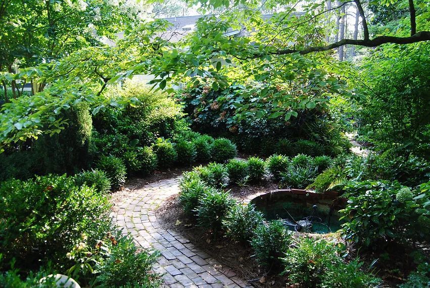 Curved stone path through lush green garden beside a small pond under leafy trees in Willow Springs, NC.