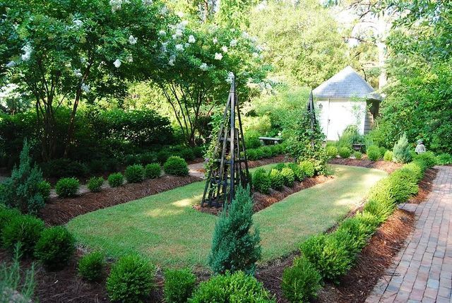 Lush garden with manicured shrubs, a brick path, and a small white gazebo among trees