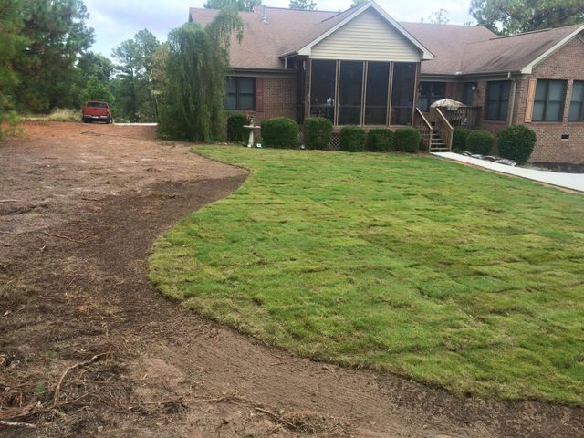 Front yard with a curved dirt driveway, green lawn, and a brick house with a covered porch in Morrisville, NC