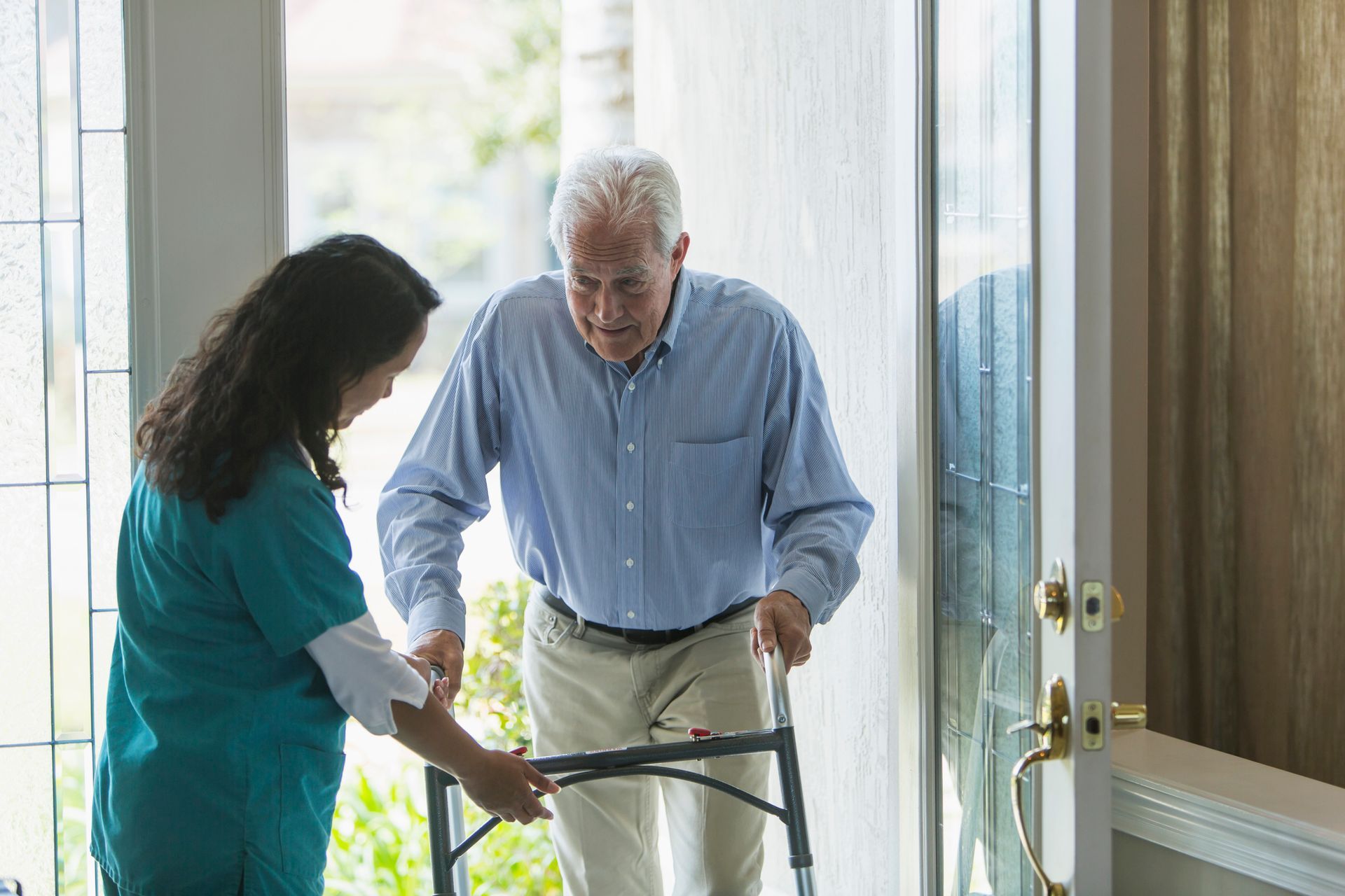 Caregiver helps an elderly man walk with a walker.