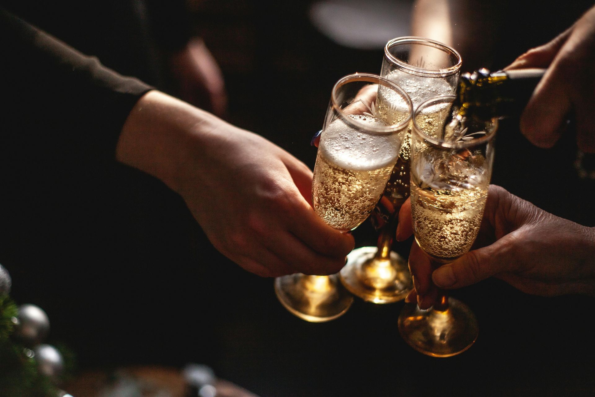 Mani che tengono dei calici da champagne, mentre viene versato, ambiente scarsamente illuminato.