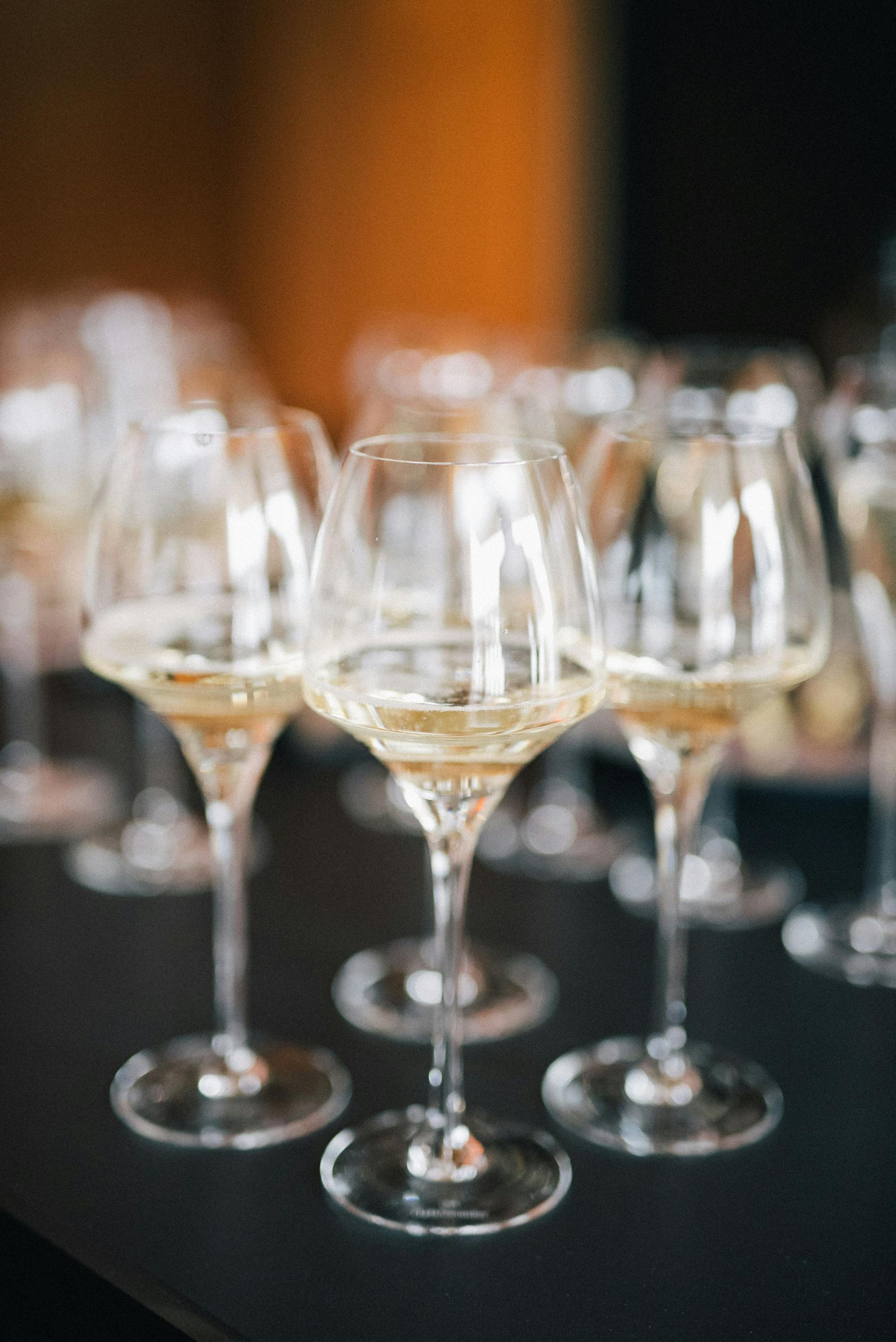 Bicchieri da vino pieni di liquido dorato su una superficie scura, sfondo sfocato.