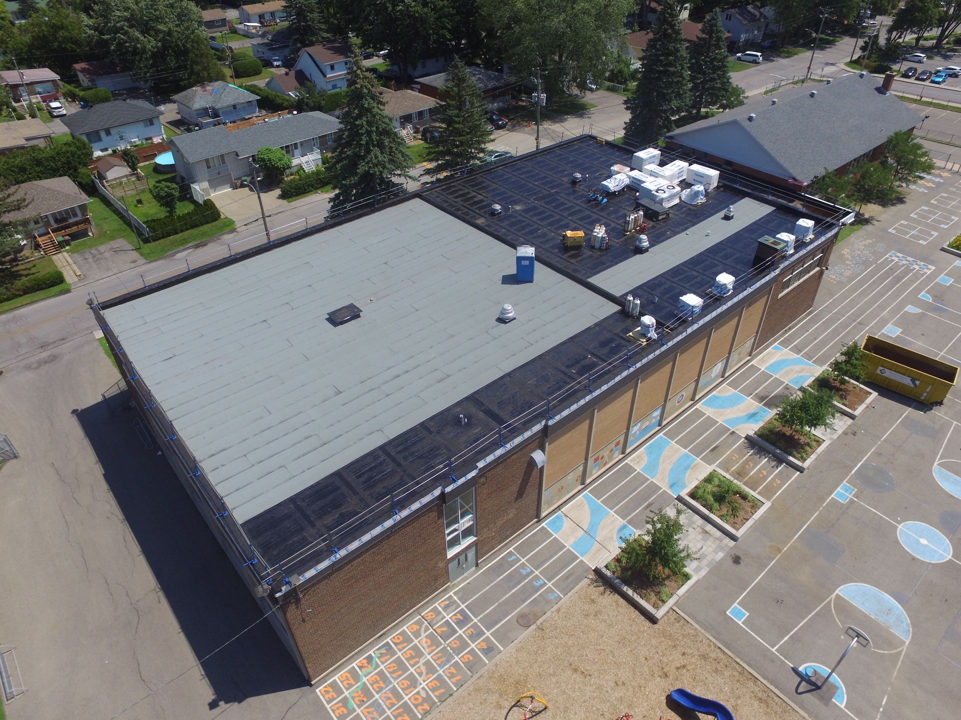 Aerial view of a large flat-roof building with a parking lot and blue-striped accessible spaces outside.