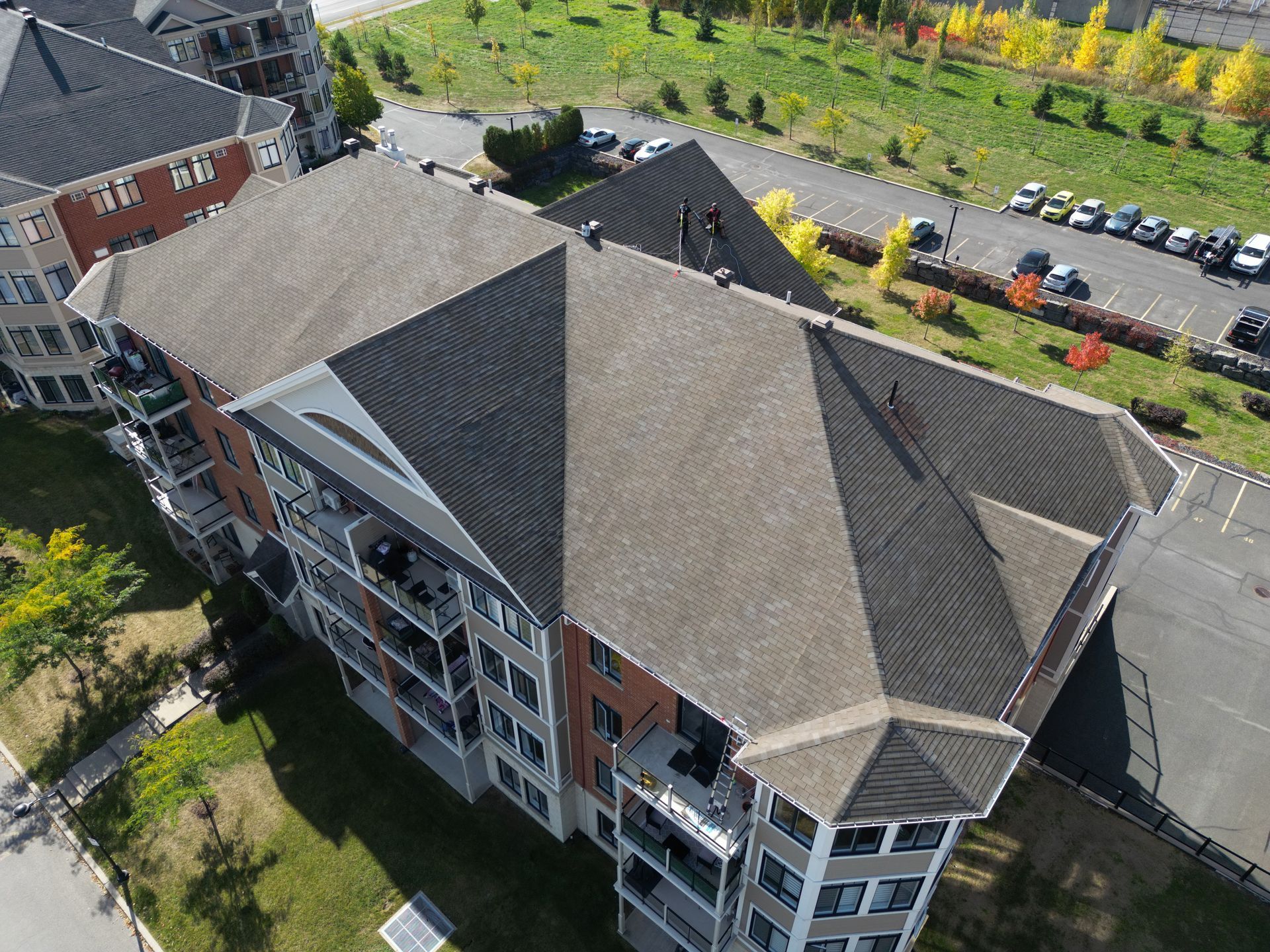 Aerial view of a modern apartment building with parking lot and trees nearby