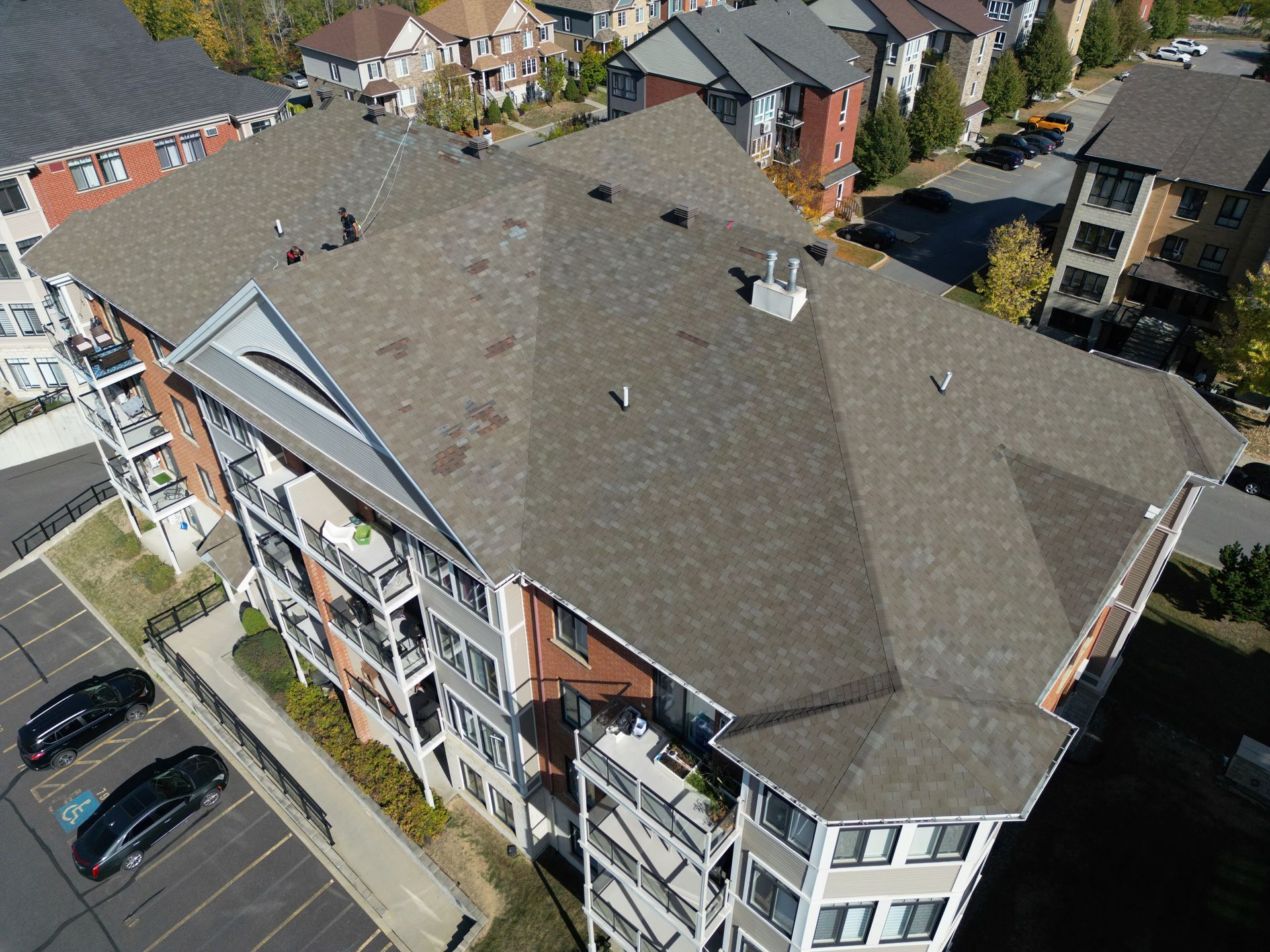 Aerial view of a gray-roofed apartment building with balconies and parked cars below.