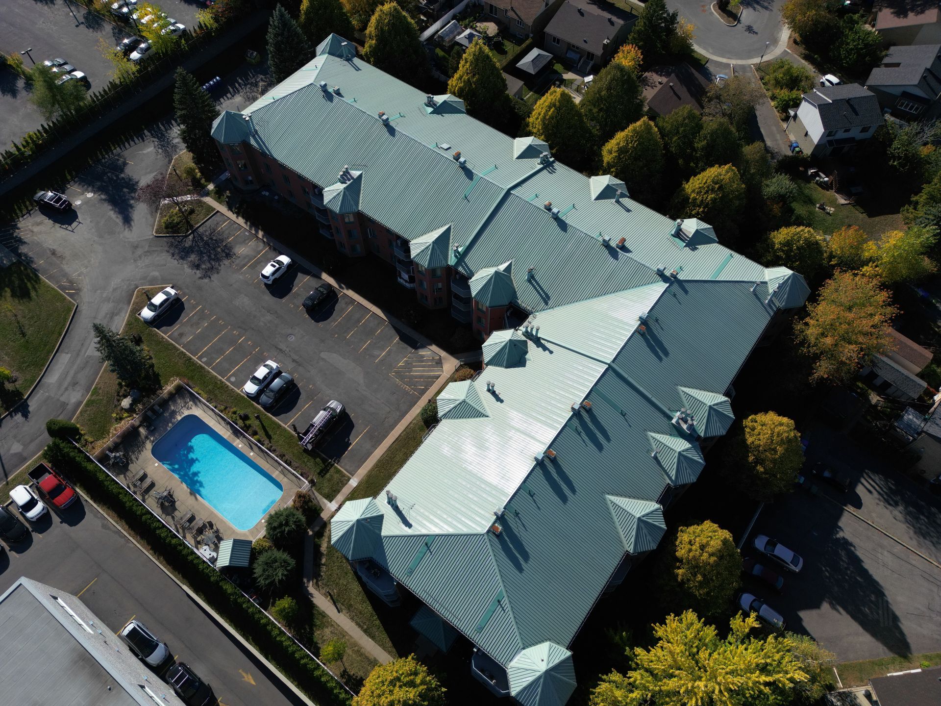 Aerial view of a large light-roofed building beside a parking lot and outdoor swimming pool
